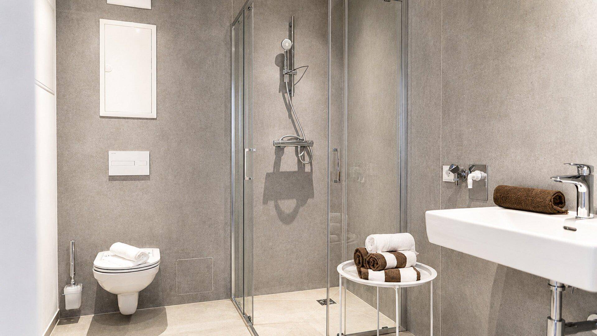 Modernes Badezimmer mit grauen Fliesen, einer Duschkabine und einem wandhängenden WC.