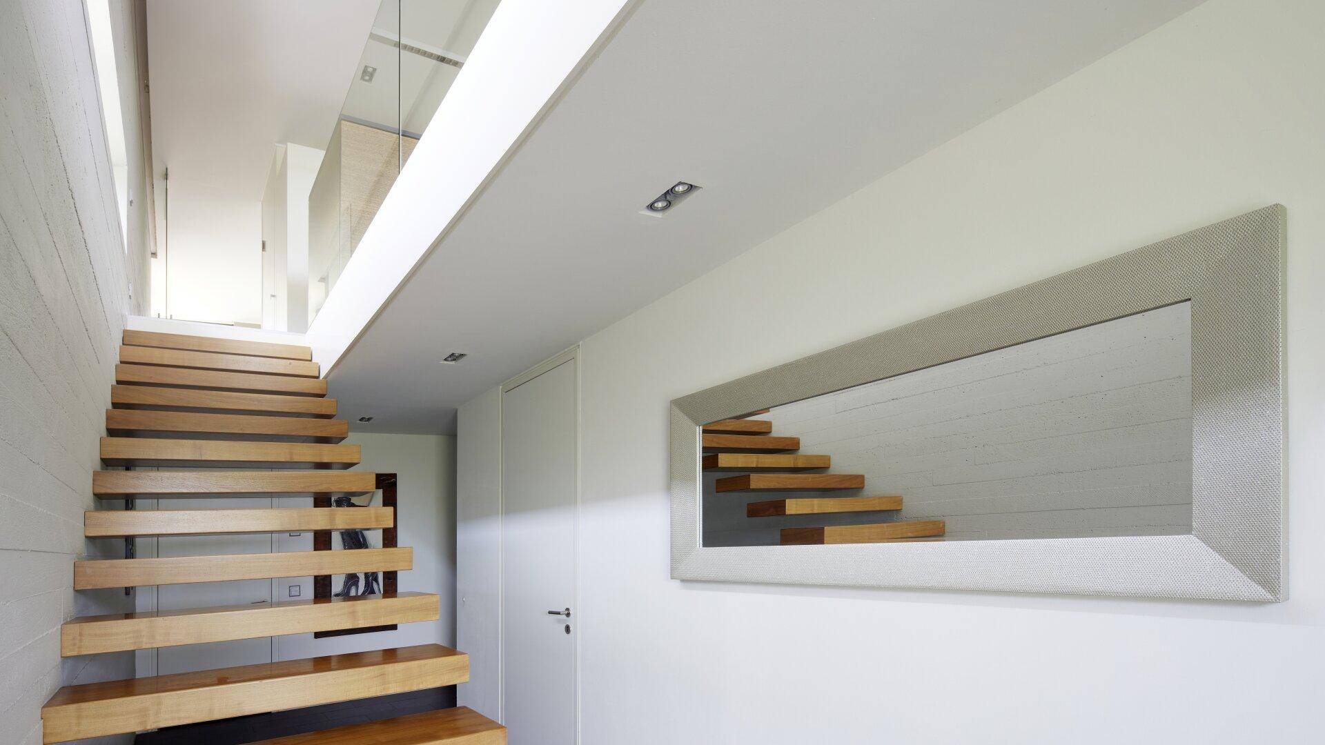 Elegante Holztreppe mit offenen Stufen und Glasgeländer, ergänzt durch einen modernen Spiegel.
