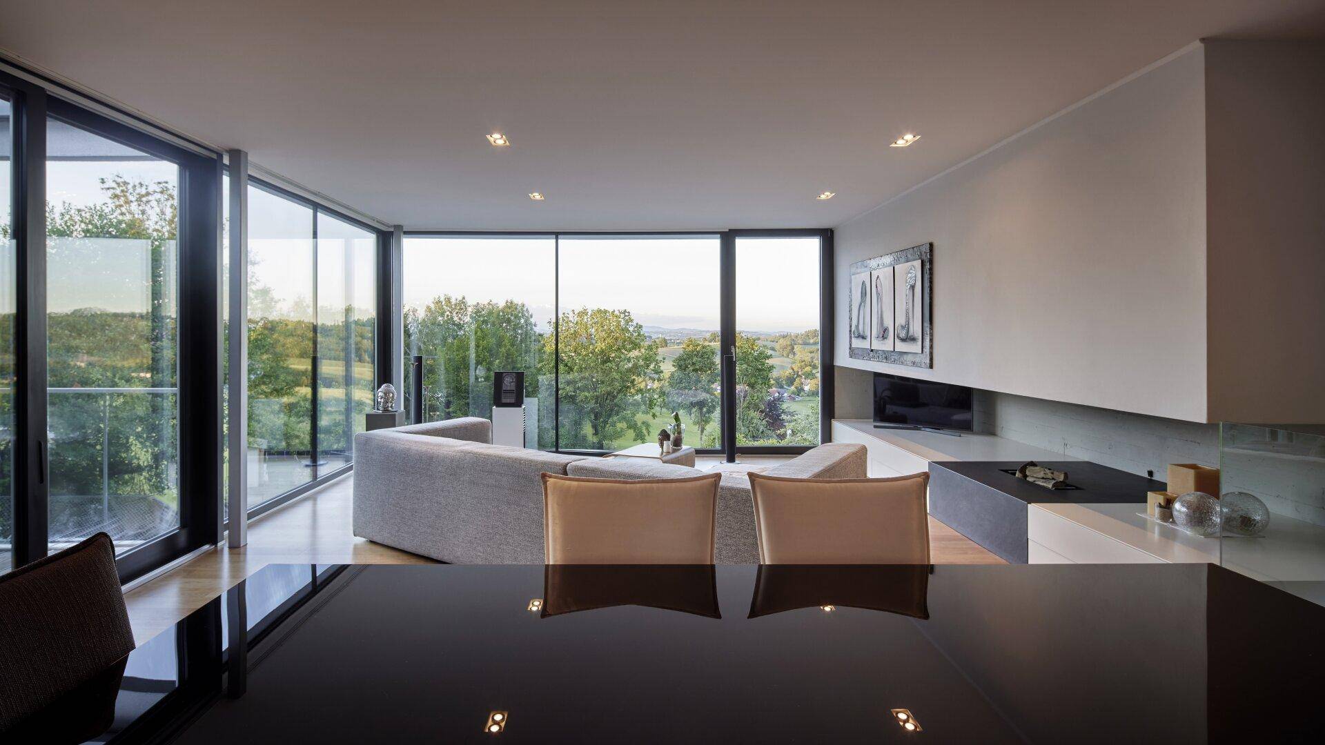 Helles Wohnzimmer mit raumhohen Fenstern und weitem Blick ins Grüne, offen gestaltet.