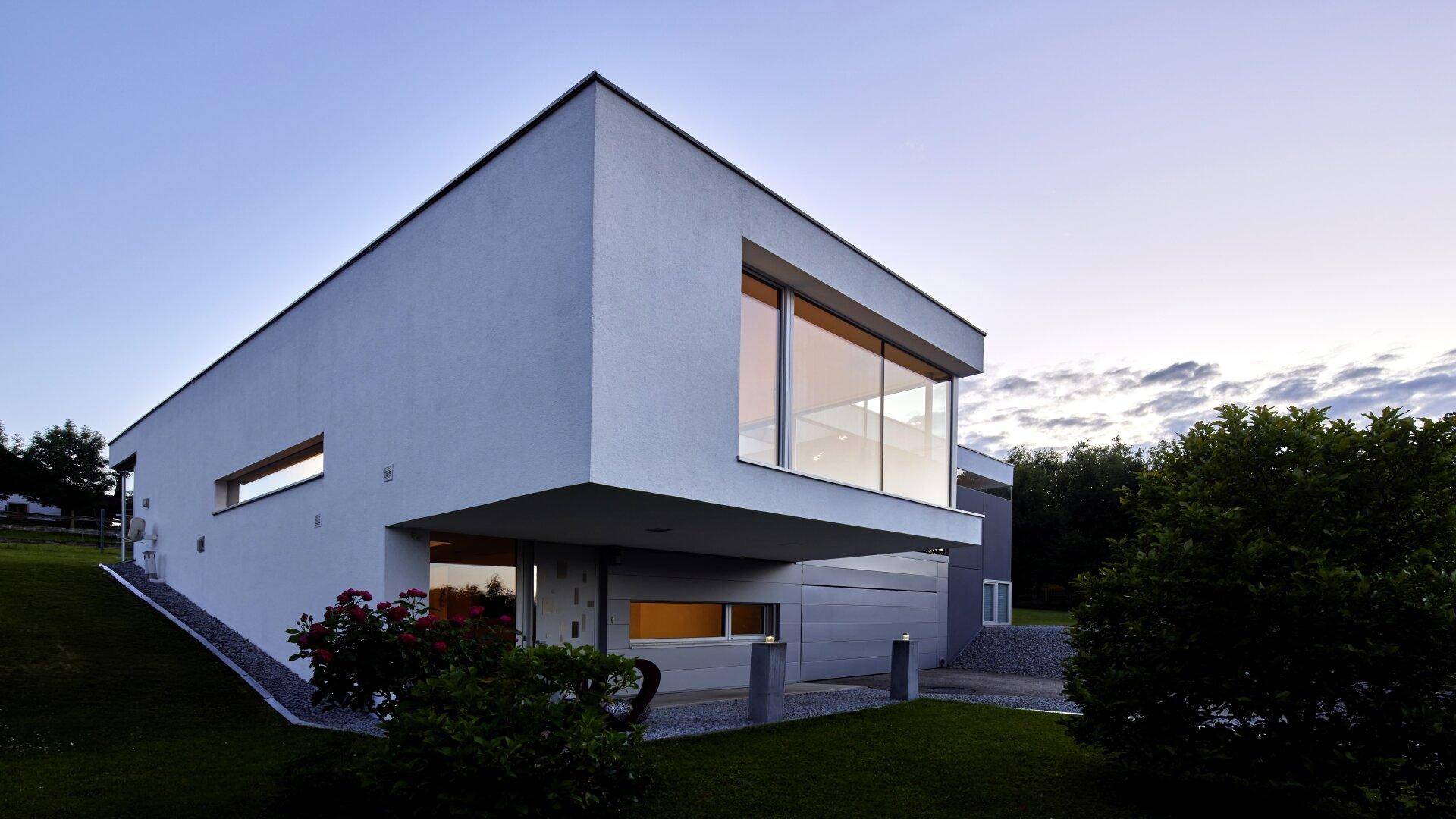 Moderne Villa mit weißer Fassade und großen Fenstern, harmonisch in die Hanglage integriert.