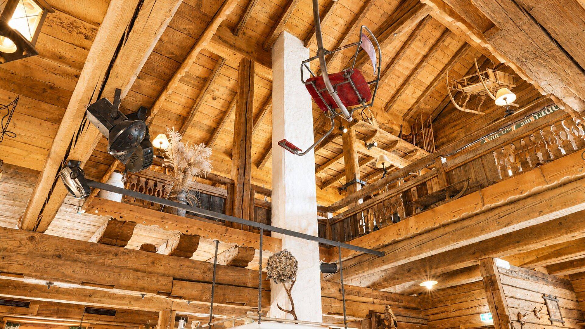 Rustikaler Innenraum mit hohen Holzdecken, sichtbaren Balken und einer dekorativen Skilift-Sesselbahn.