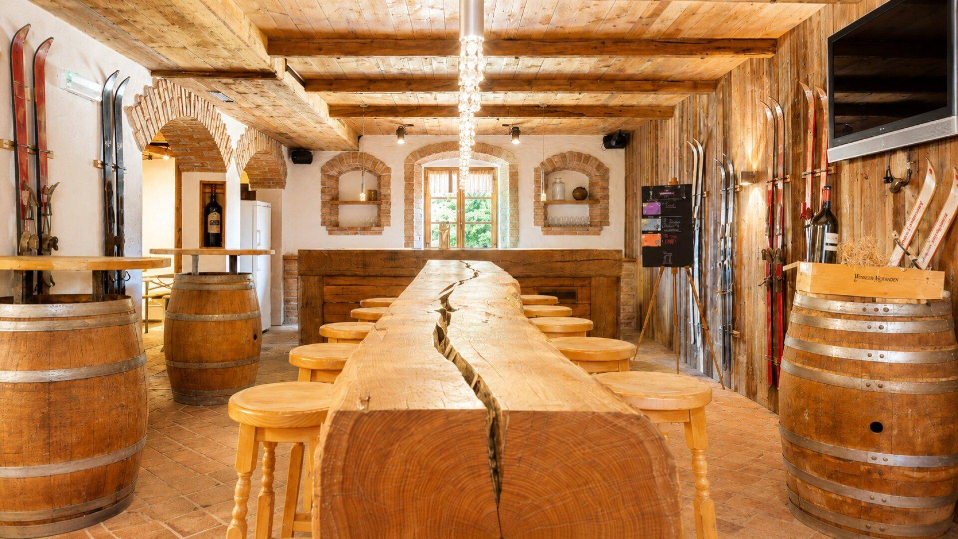 Geräumiger Barbereich mit langer Holztheke, Weinfässern und Skiern als Dekoration in rustikalem Ambiente.