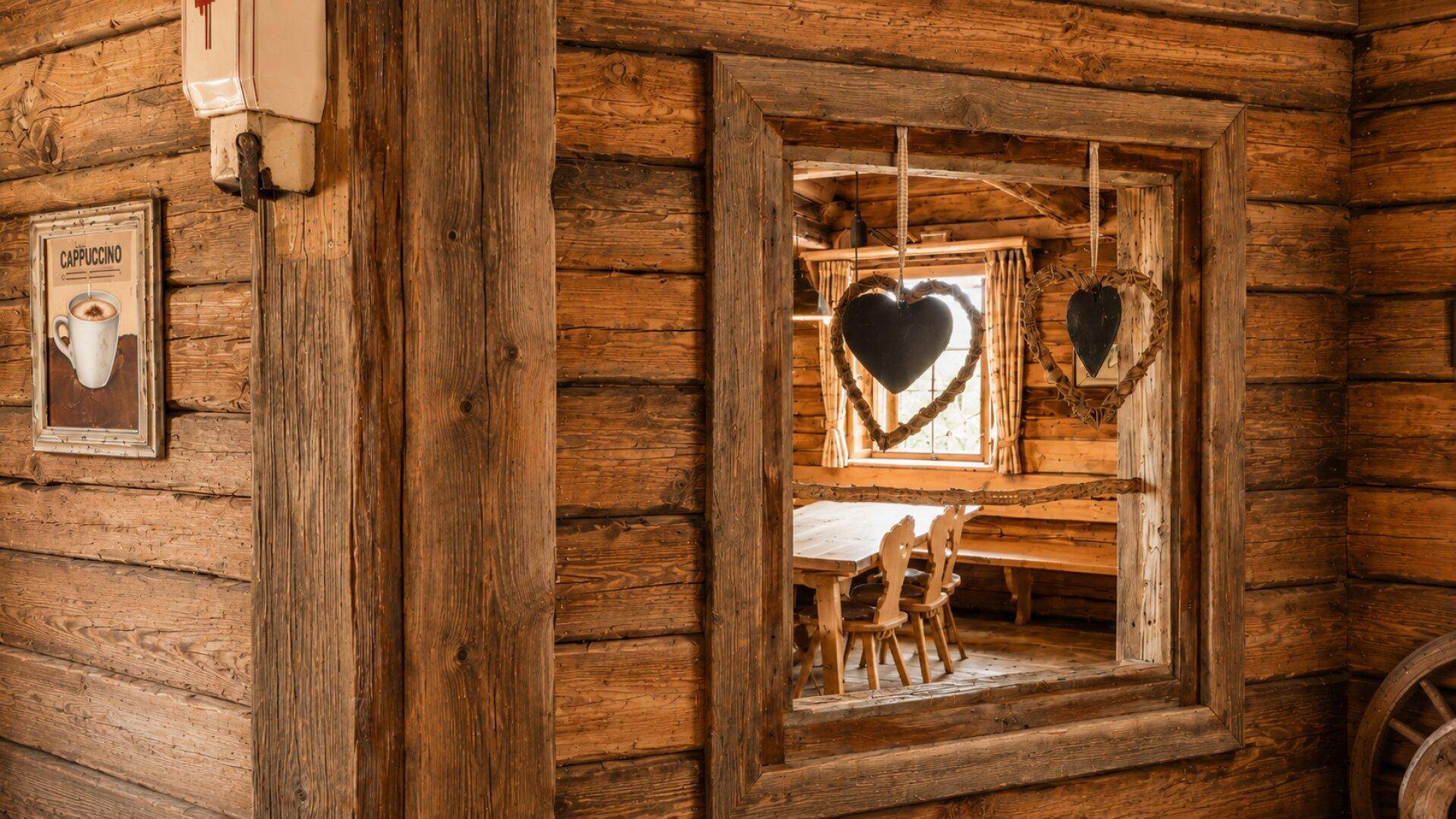 Detailansicht einer Holzwand mit einem Durchbruchfenster, das den Blick in einen rustikalen Essbereich freigibt.