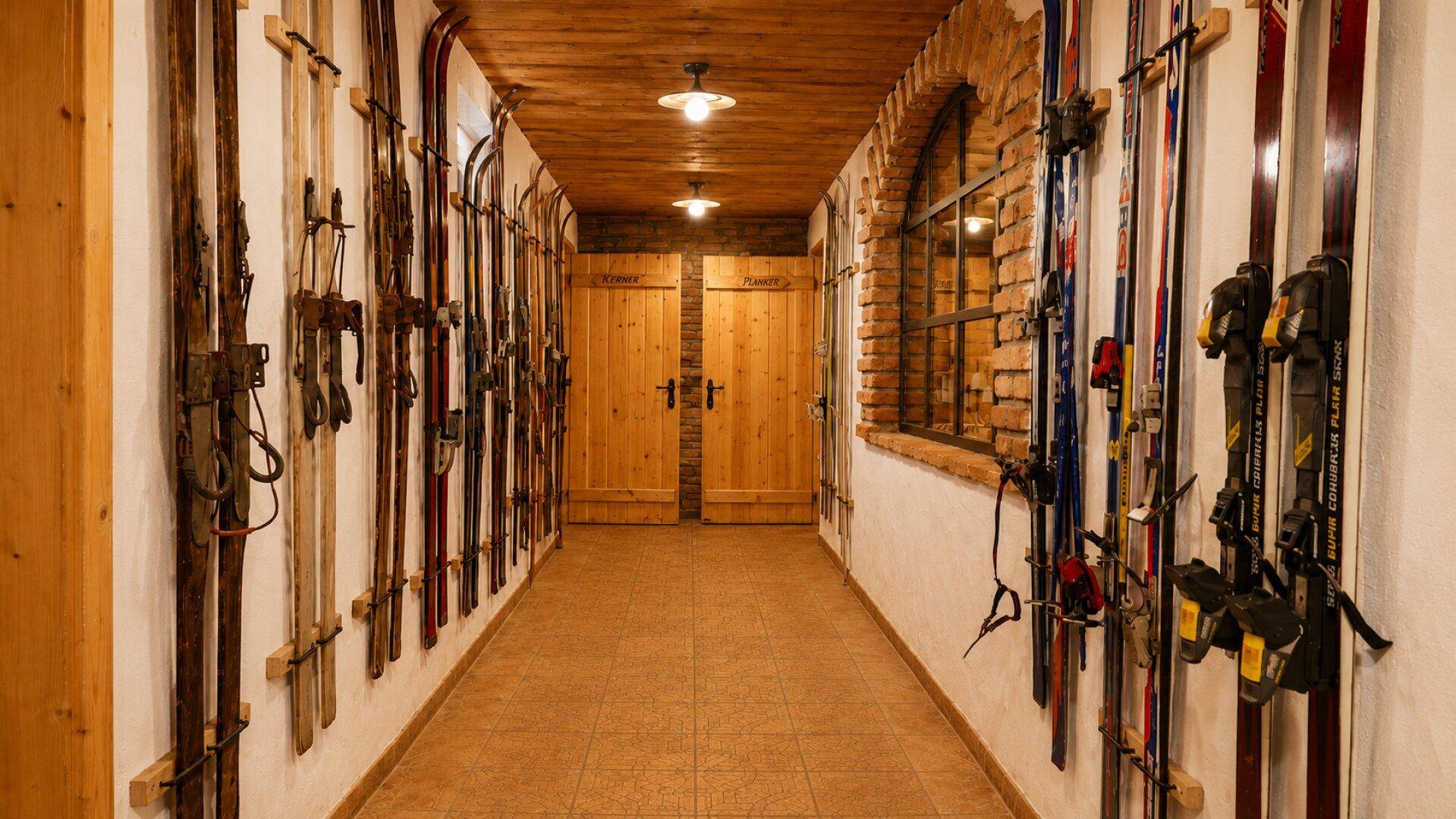 Langer Flur mit beidseitiger Skiaufbewahrung, Holztüren am Ende und einem Bogenfenster aus Ziegeln.