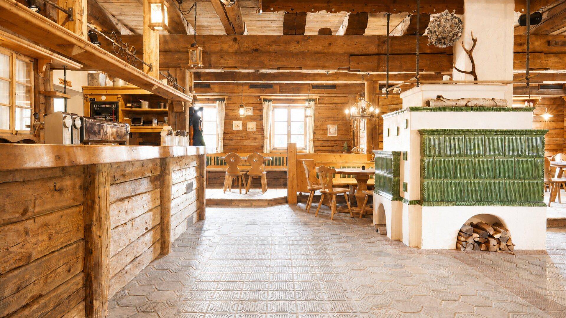 Geräumiger Essbereich in einer Holzhütte mit einem großen grünen Kachelofen und rustikalen Holzmöbeln.