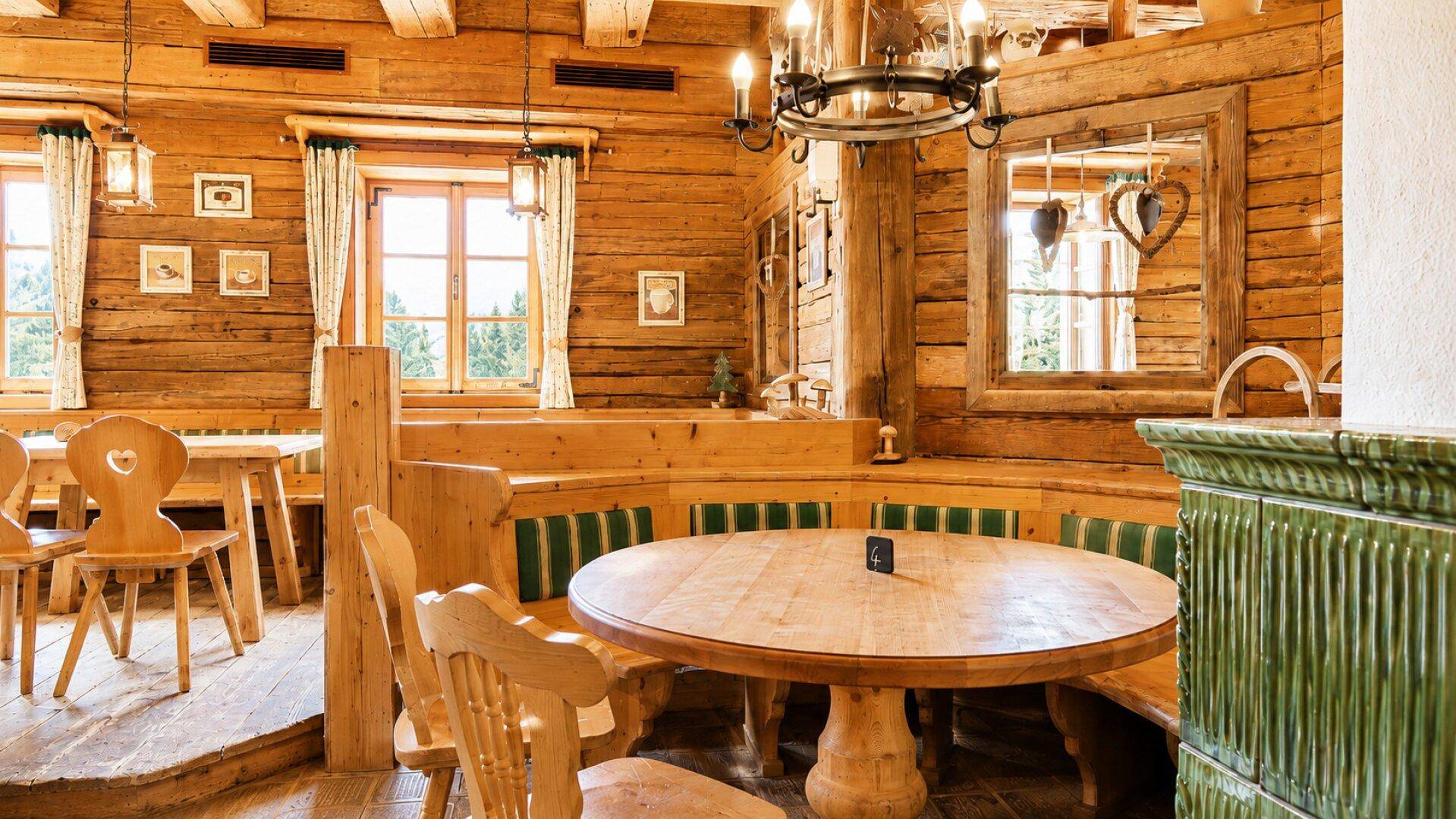 Rustikaler Essbereich mit runden Holztischen, eingebauten Sitzbänken und einem traditionellen Kachelofen.