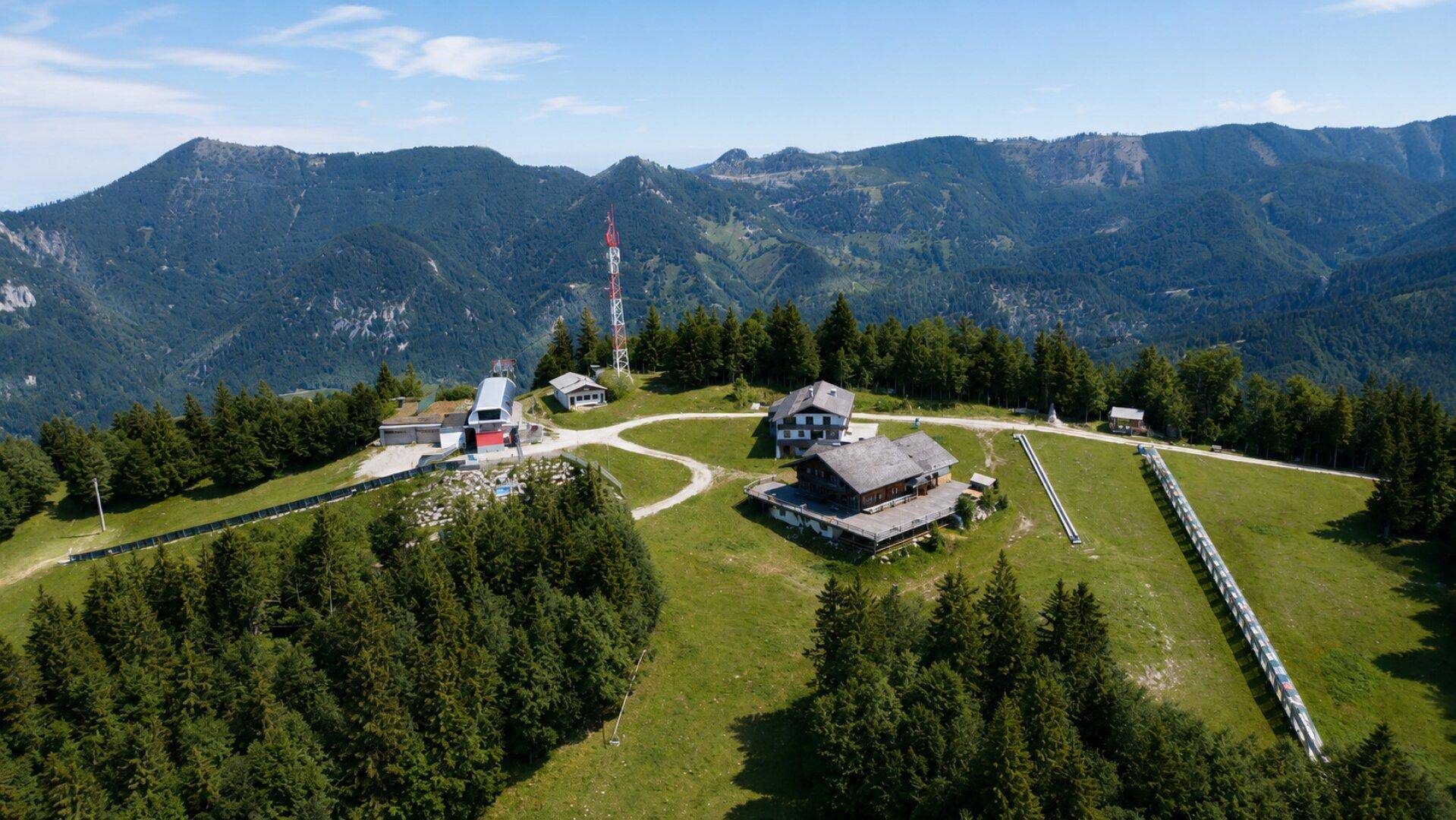 Weitläufige Luftaufnahme des Berggipfels mit mehreren Gebäuden, Skilift und einer langen Skipiste.
