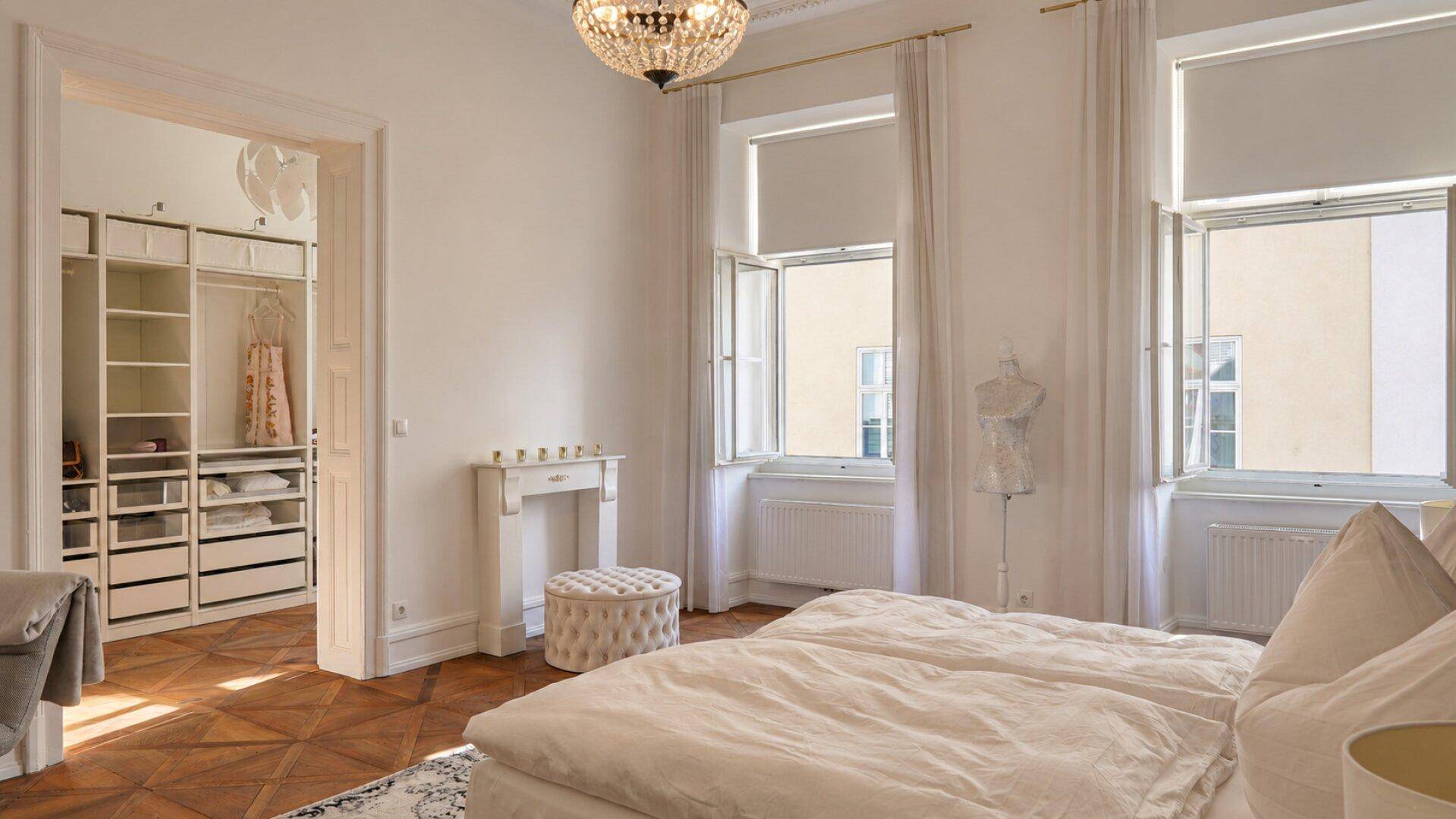 Geräumiges Schlafzimmer mit Zugang zu einem begehbaren Kleiderschrank und hohen Fenstern.