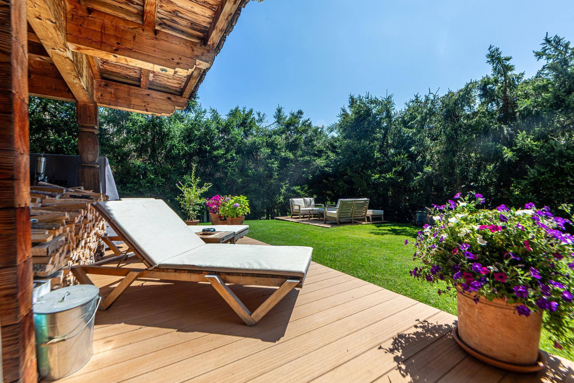 Entspannungsbereich im Garten mit Liegestühlen auf einem Holzdeck und Blick auf die Berge.