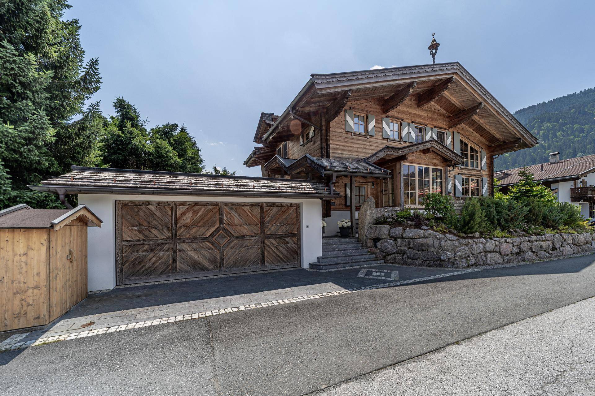 Traditionelles Holzchalet mit integrierter Doppelgarage und gepflegter Steinfassung am Hang.