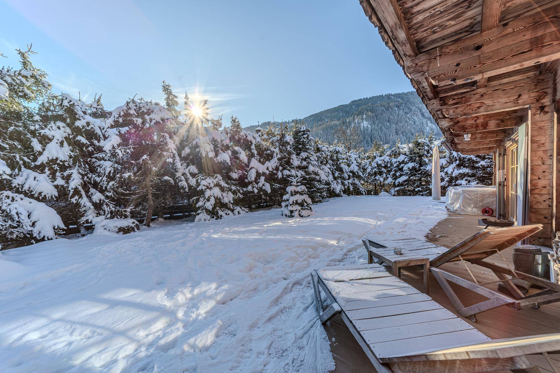 Sonniger Wintergarten mit schneebedeckten Bäumen und Liegestühlen auf der Terrasse.