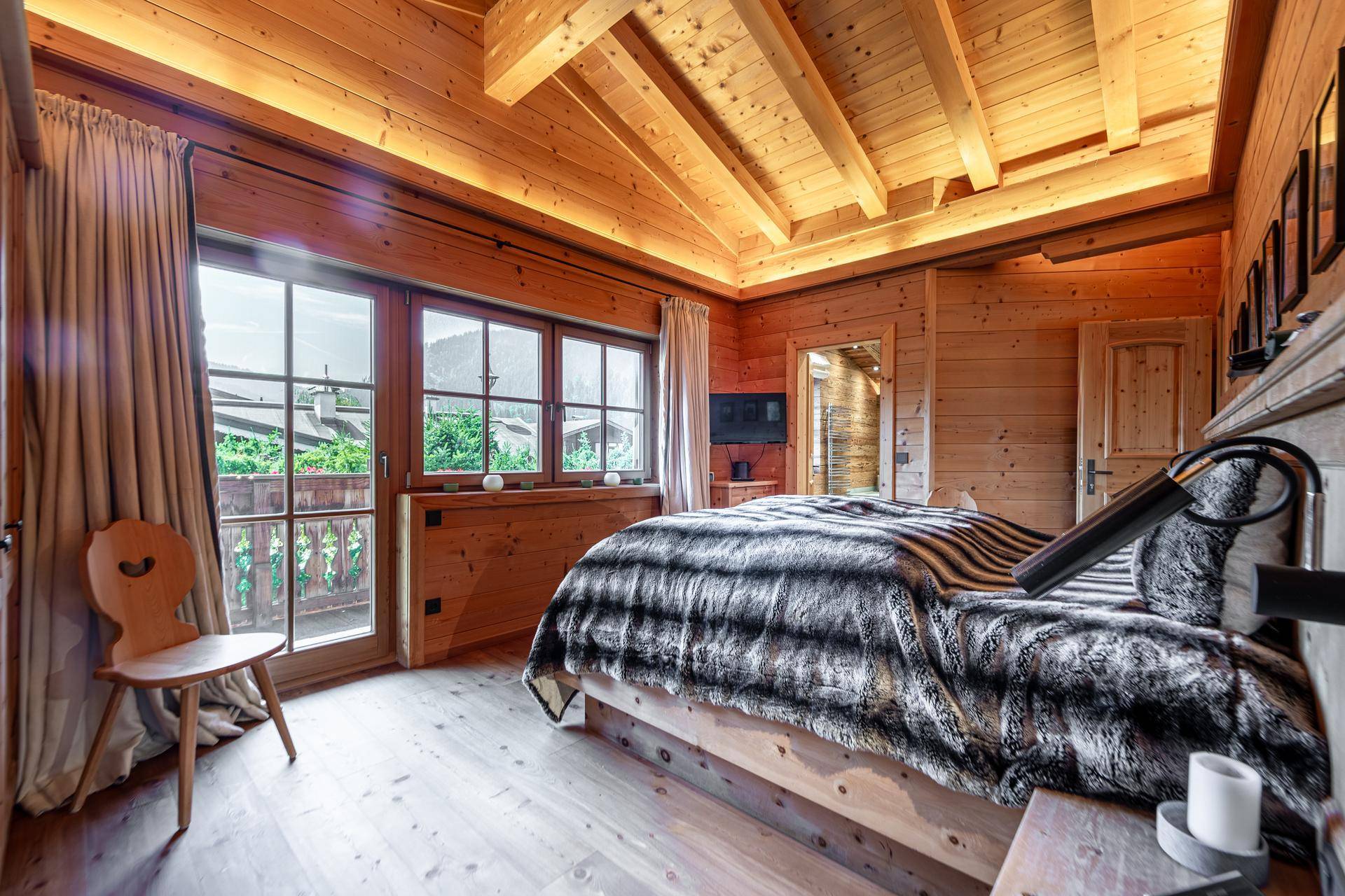 Schlafzimmer im Chalet-Stil mit Holzwänden, Holzboden und Zugang zum Balkon mit Bergblick.