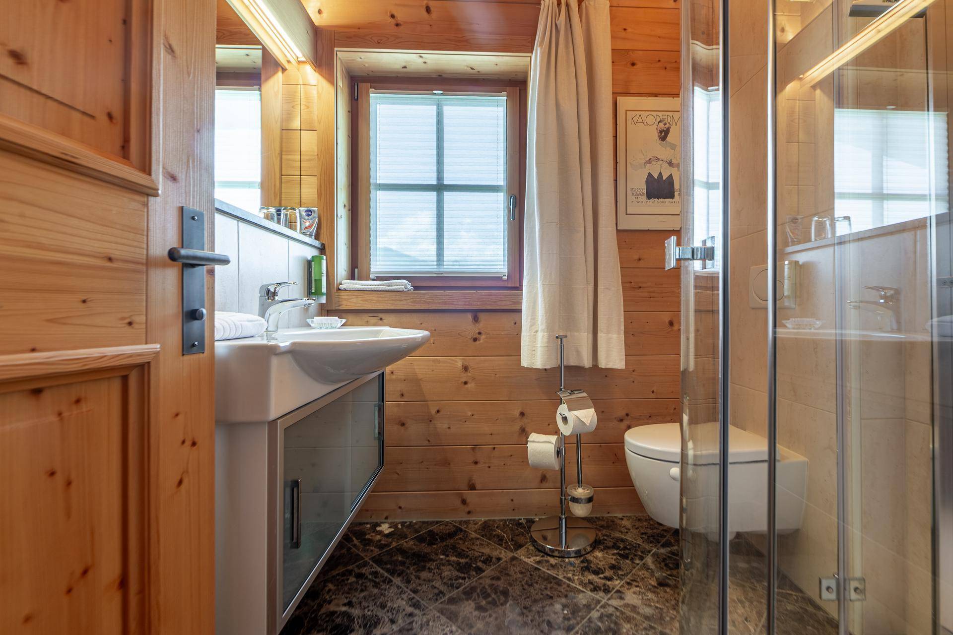 Badezimmer mit Holzwänden, Badewanne, Dusche und Fenster für natürliches Licht.