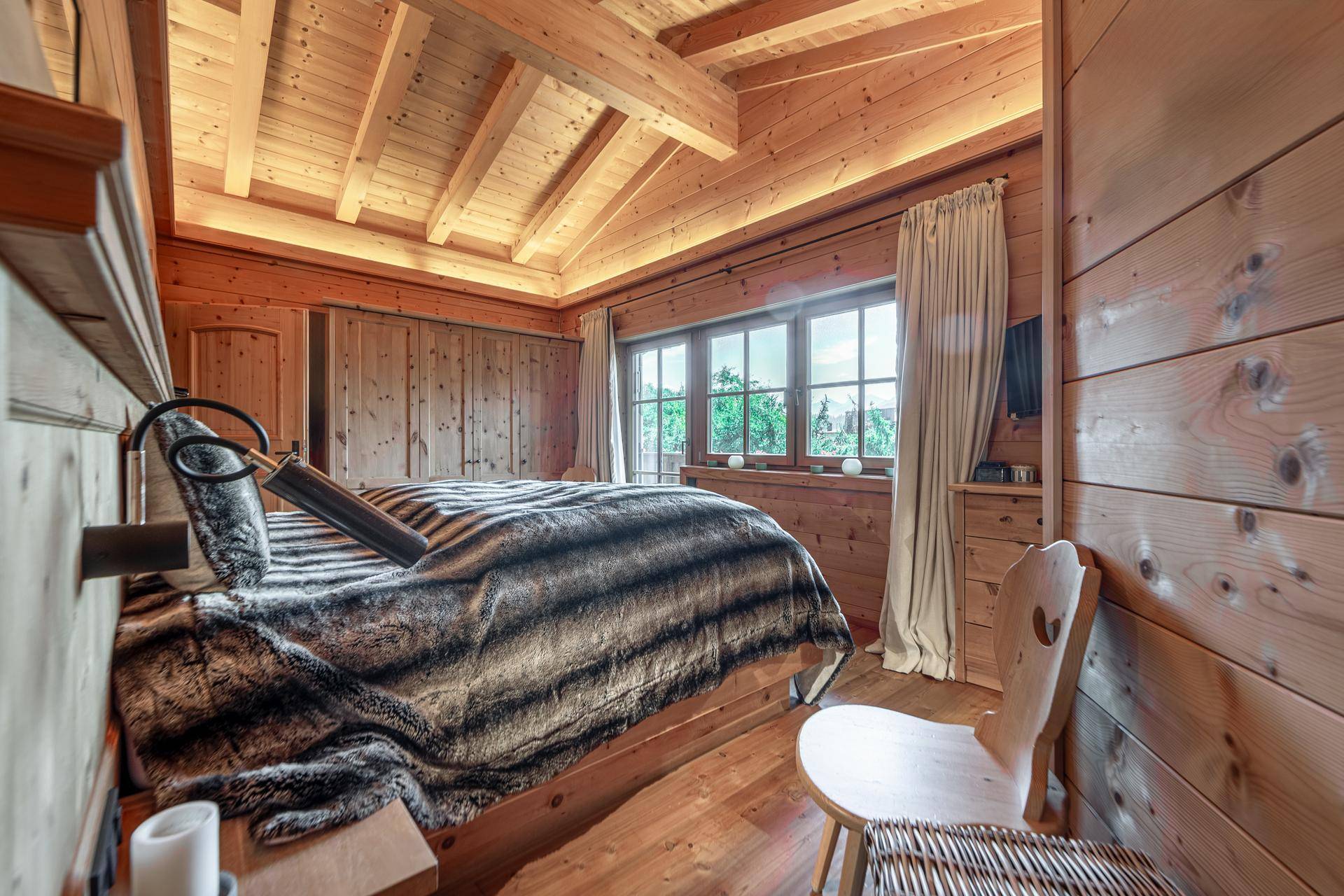 Gemütliches Schlafzimmer mit Holzwänden, Holzboden und einem großen Fenster mit Blick ins Grüne.
