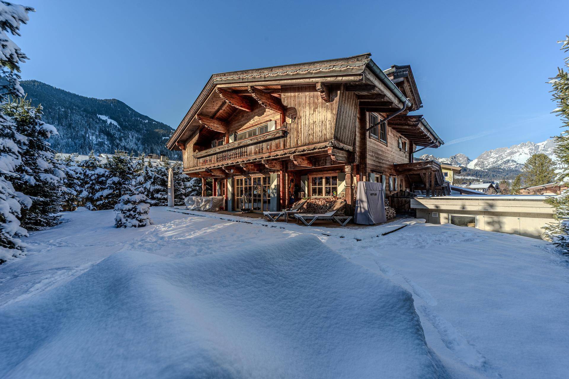 Traditionelles Holzchalet im Winter mit schneebedeckter Landschaft und klarem Himmel.