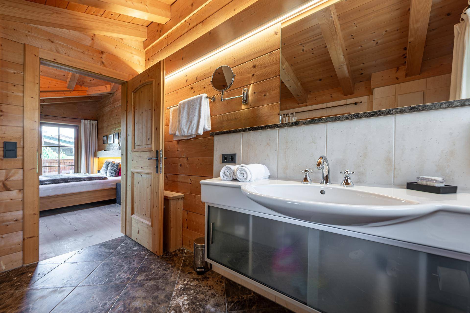 Badezimmer mit Einzelwaschbecken, großem Spiegel und Holzvertäfelung, offen zum Schlafzimmer.
