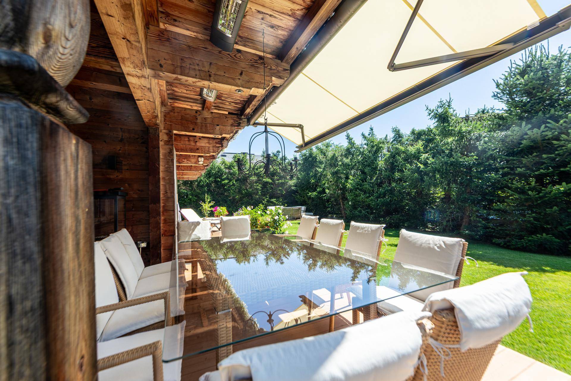 Überdachter Terrassenbereich mit großem Glastisch und bequemen Stühlen, ideal für Mahlzeiten im Freien.