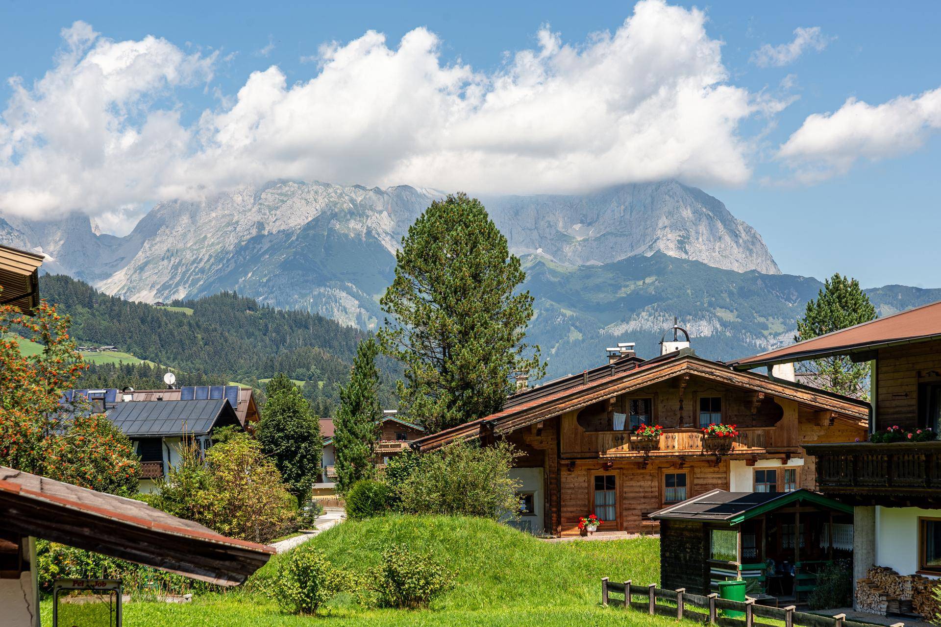Malerische Berglandschaft mit traditionellen Häusern und üppigem Grün unter blauem Himmel.