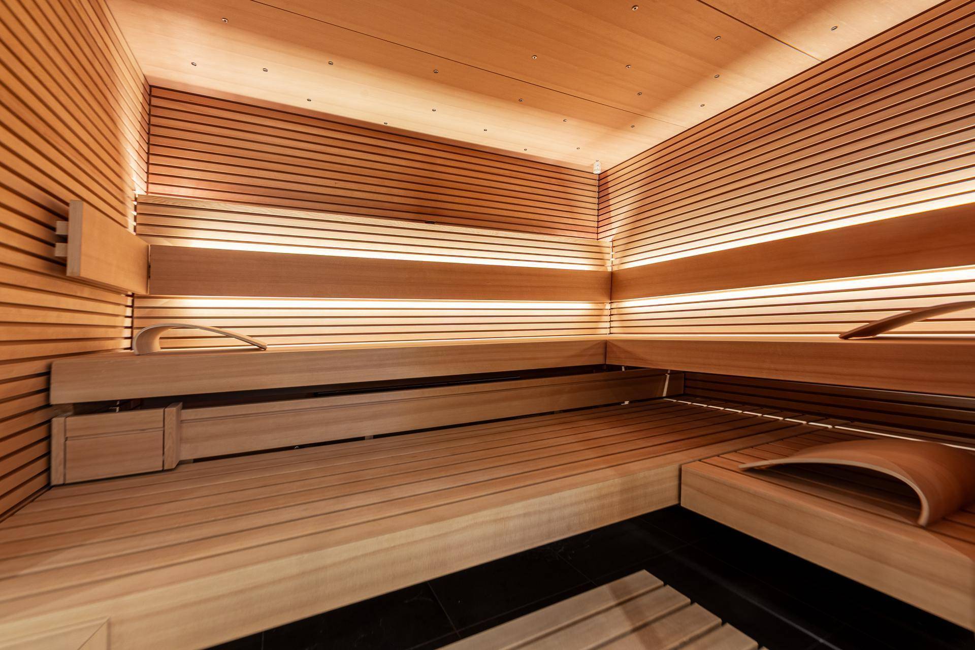 Moderne Holzsauna mit mehreren Bänken und indirekter Beleuchtung für Entspannung.