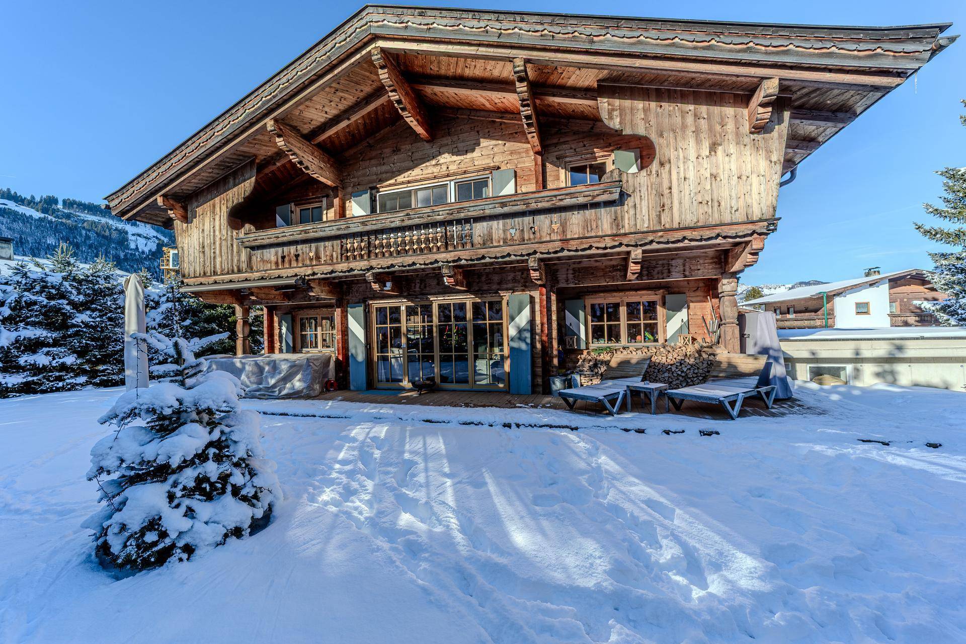 Traditionelles Holzchalet im Winter mit schneebedeckter Terrasse und Garten.