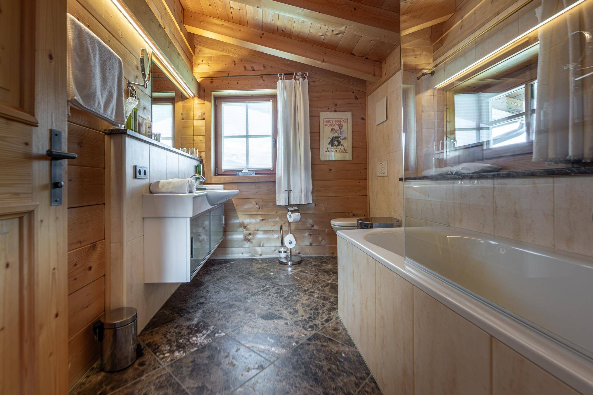 Badezimmer mit Badewanne, Dusche, Einzelwaschbecken und Holzvertäfelung im Chalet-Stil.