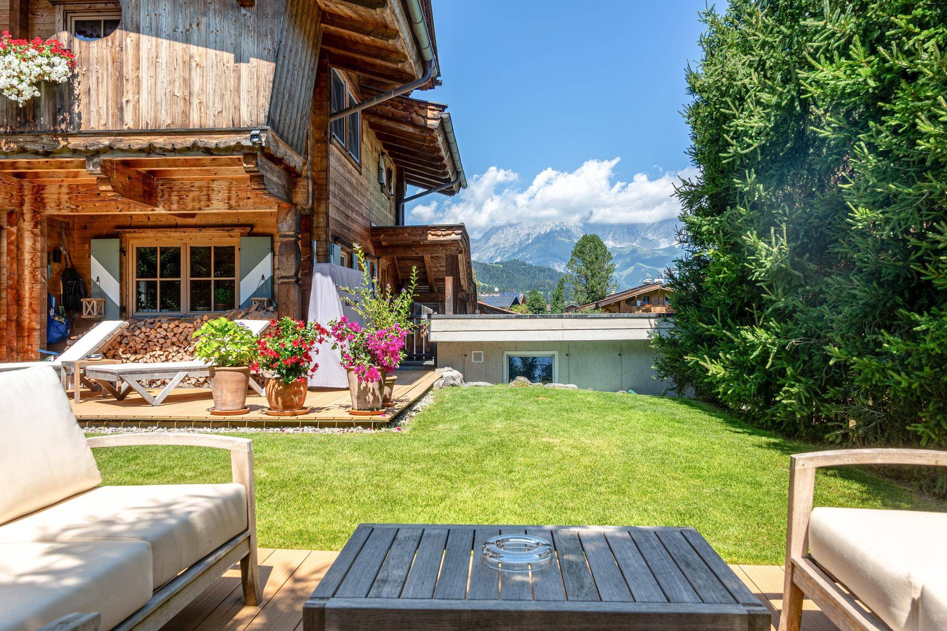 Sonniger Gartenbereich mit Lounge-Möbeln auf einem Holzdeck und weitem Bergblick.