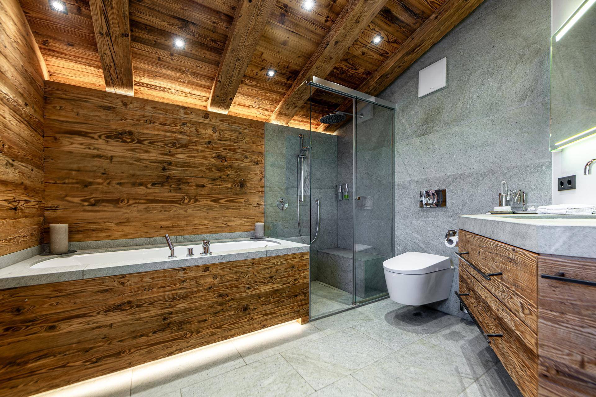 Geräumiges Badezimmer mit Badewanne, Glasdusche, Wand-WC und Holz- und Steinakzenten.