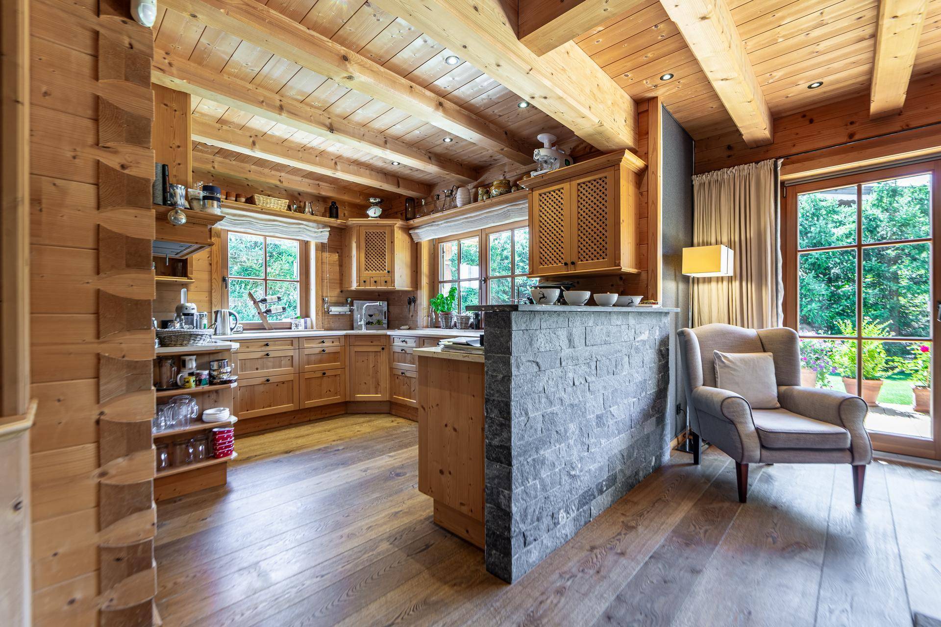 Rustikale Holzküche mit Steinwand, integrierten Geräten und offenem Übergang zum Wohnbereich.