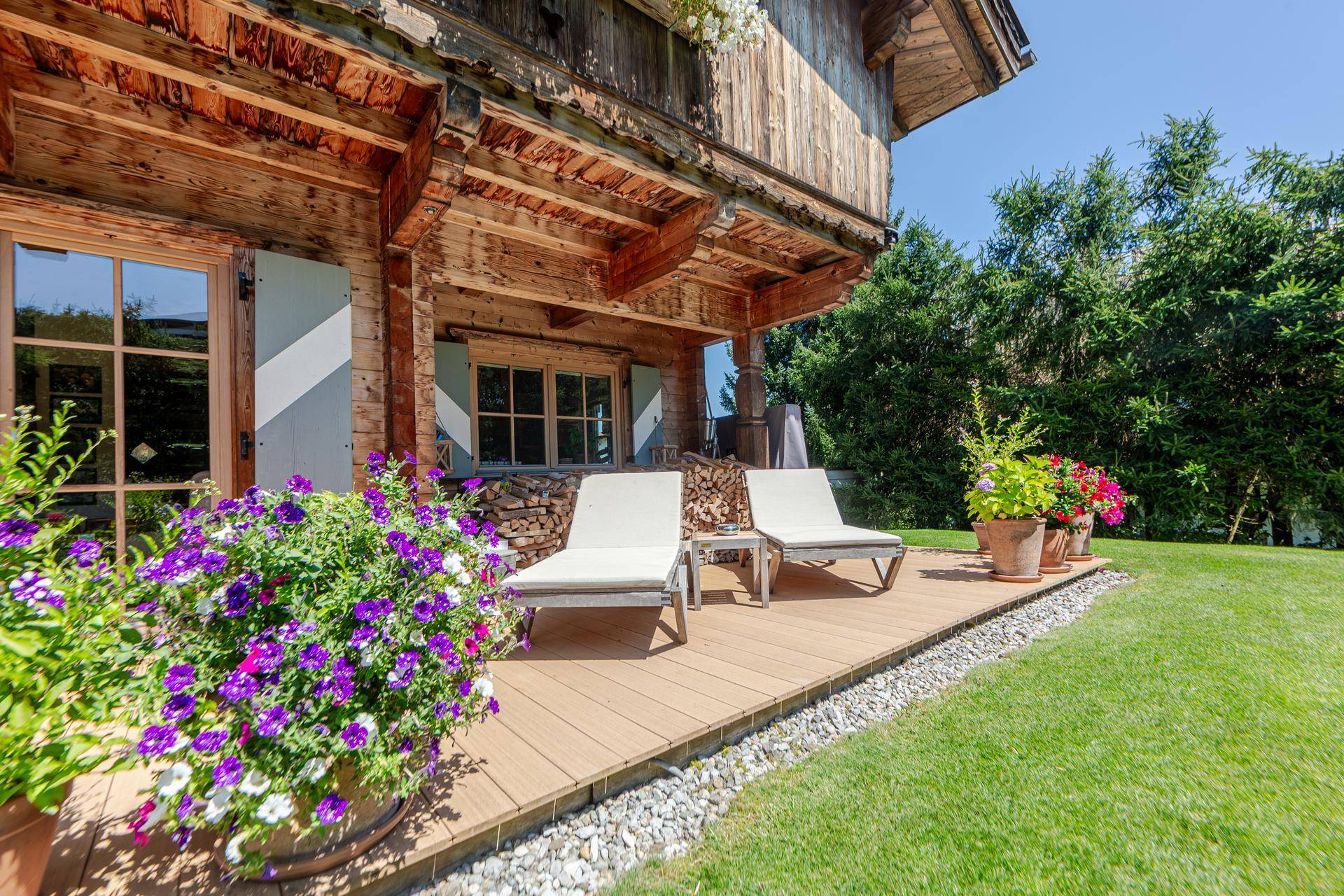 Sonniger Terrassenbereich mit Liegestühlen und bunten Blumen vor dem Holzchalet.