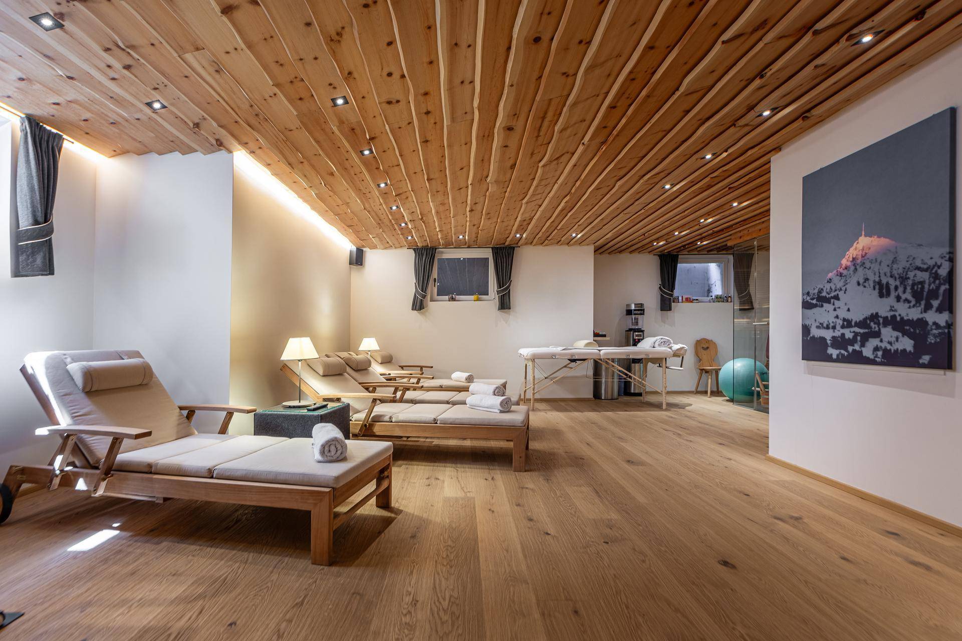 Geräumiger Wellnessbereich mit Liegestühlen, Massageliegen und Holzbalkendecke.