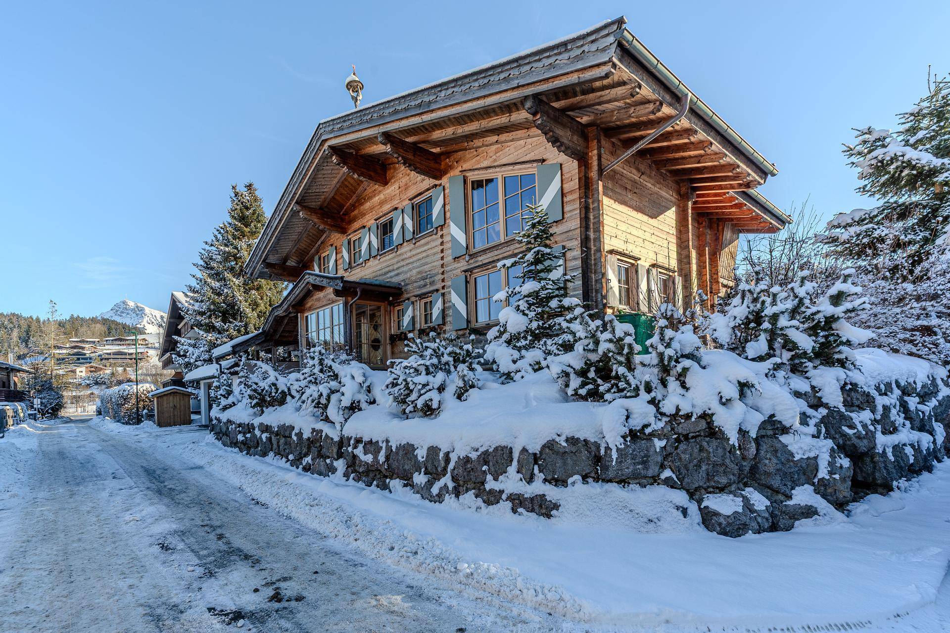 Charmantes Holzchalet im Winter, umgeben von schneebedeckten Bäumen und Bergen.