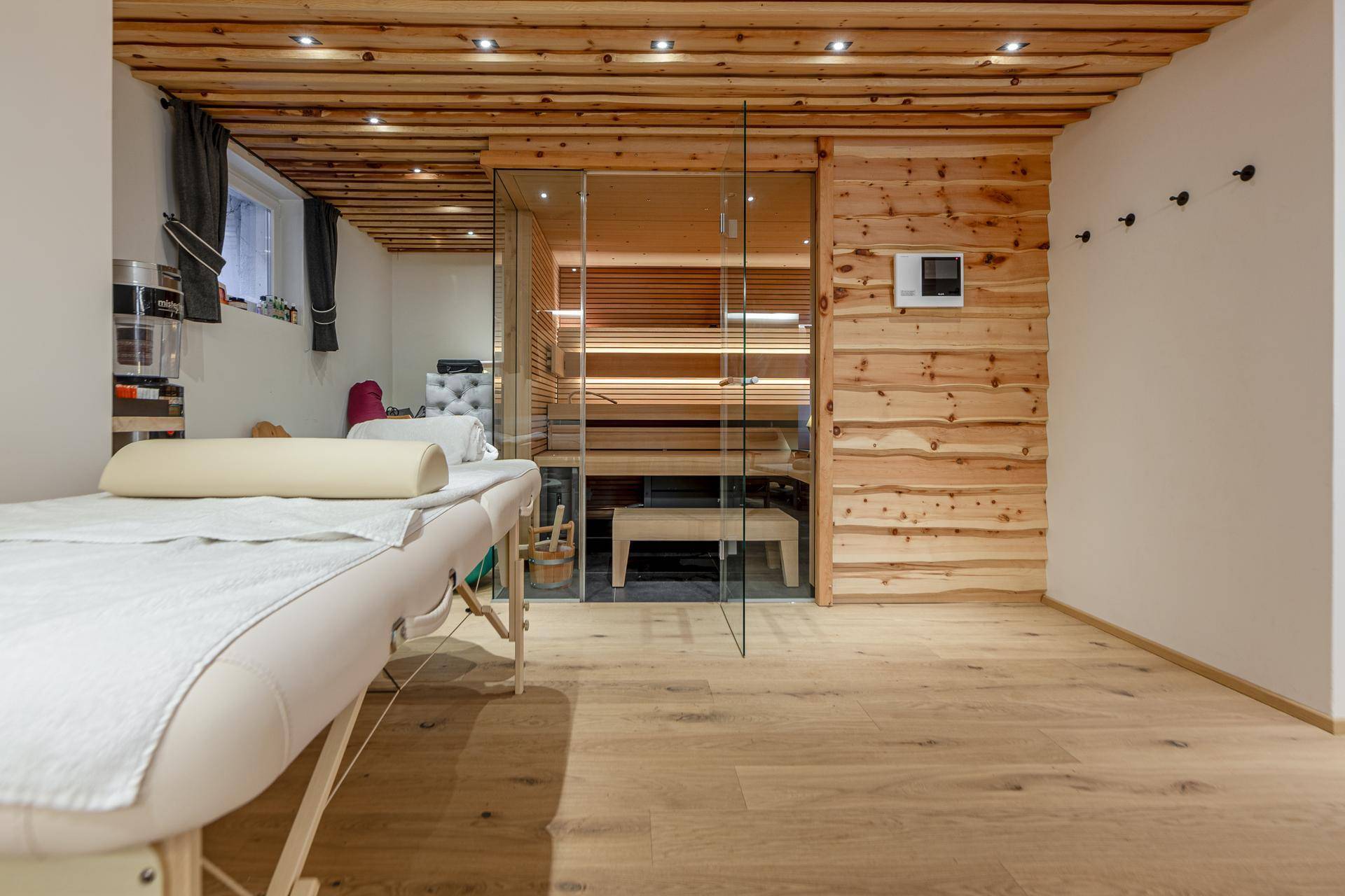 Entspannungsbereich mit Massageliege und Blick auf die moderne Sauna mit Glasfront.