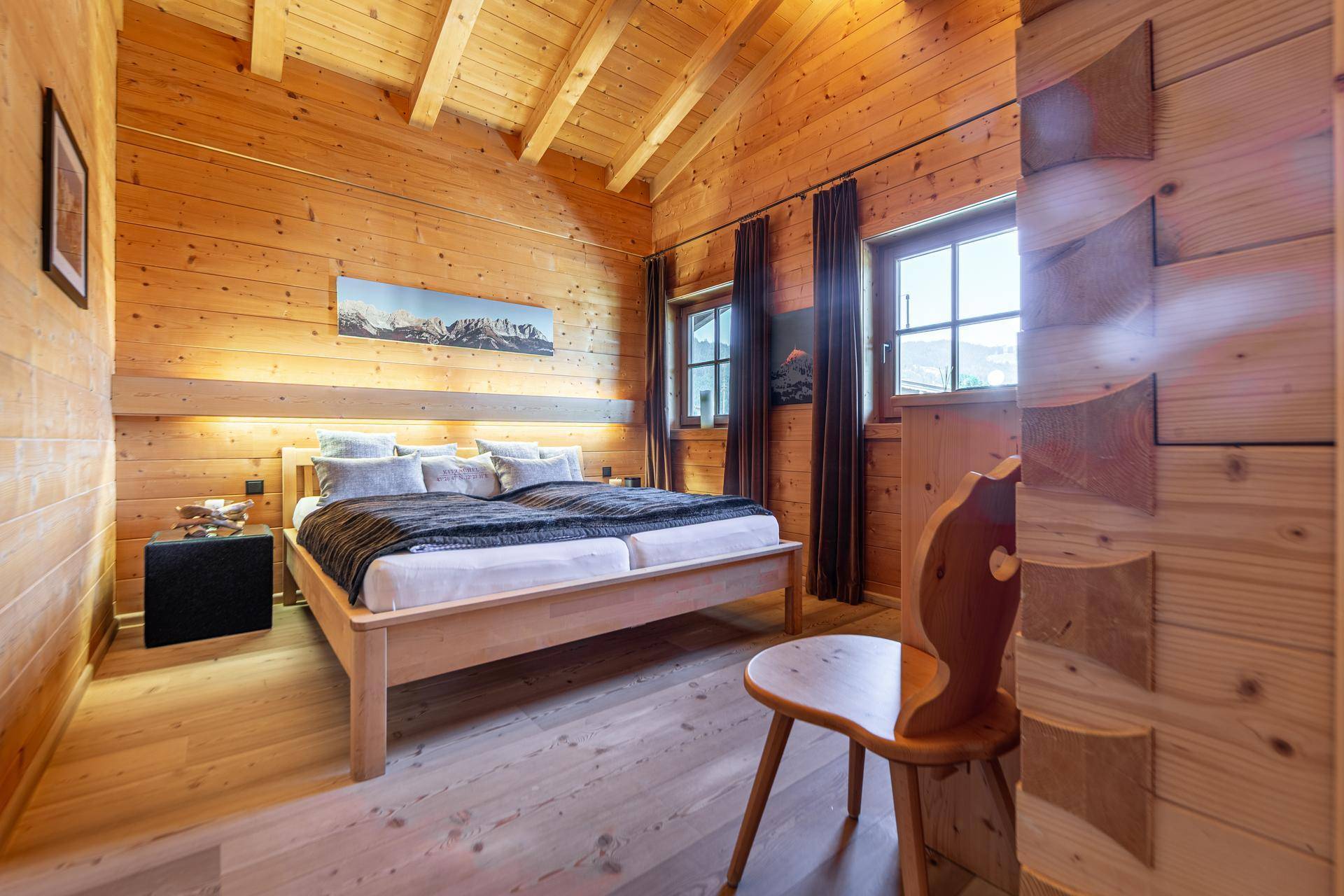 Helles Schlafzimmer mit Holzwänden, Holzboden und einem großen Doppelbett mit Bergblick.