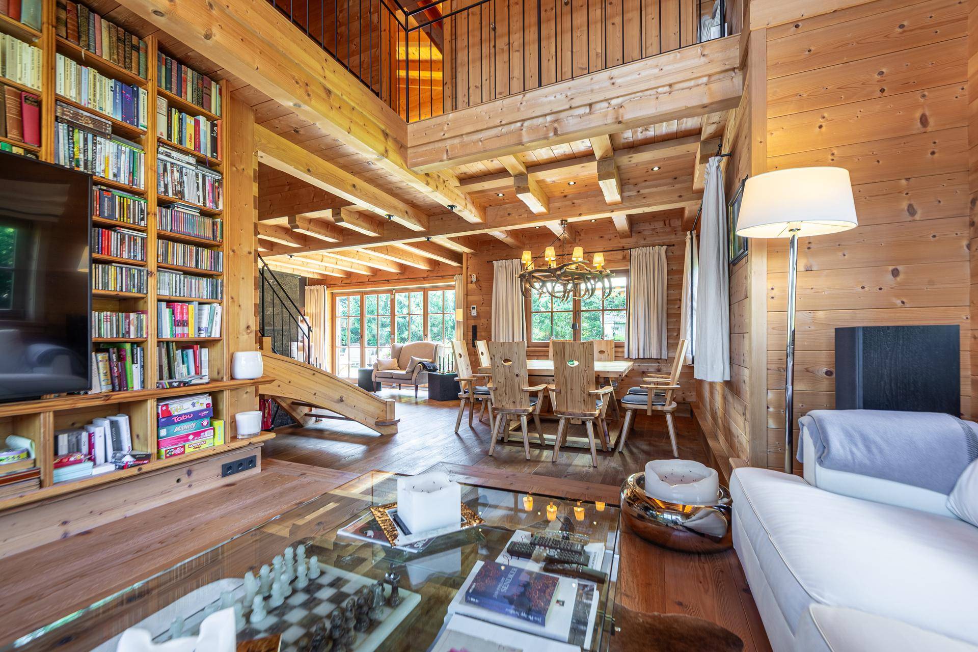 Offener Wohn-Essbereich mit Bücherregal, Holzbalkendecke und Treppe zur oberen Etage.