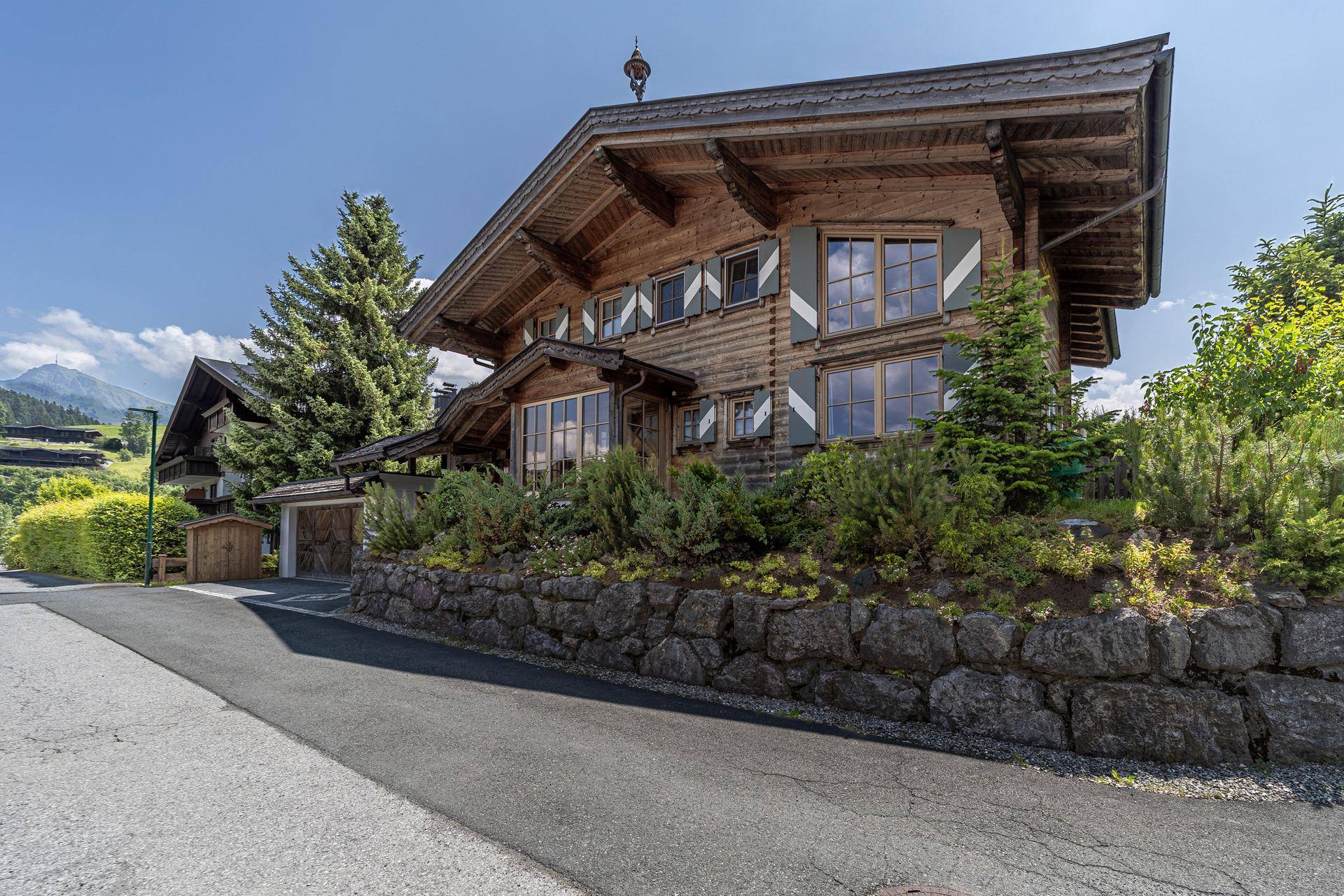 Charmantes Holzchalet mit grünen Fensterläden und einer Natursteinmauer in alpiner Umgebung.