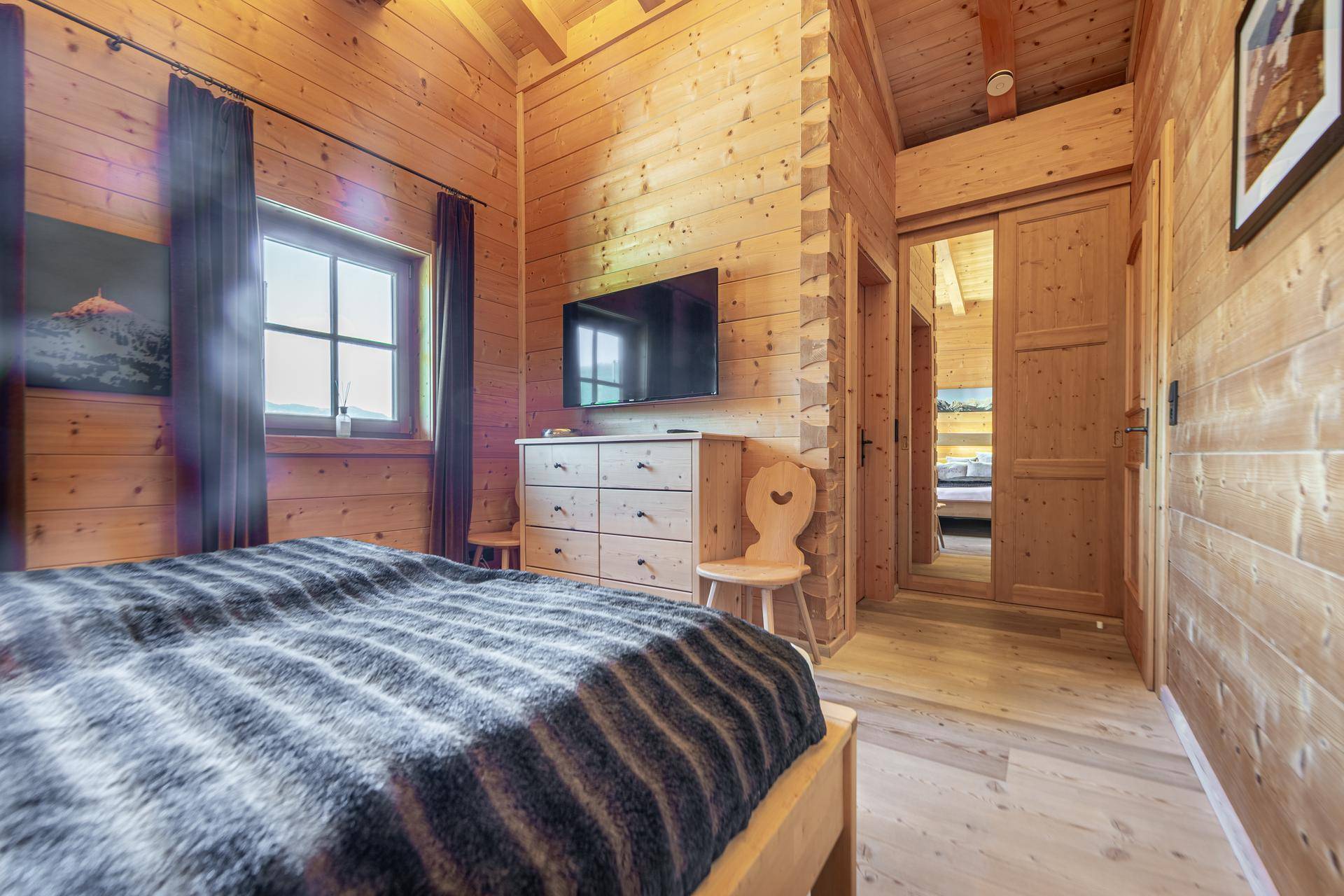 Schlafzimmer mit Holzwänden, Holzboden und einem Fernseher, offen zu einem weiteren Raum.