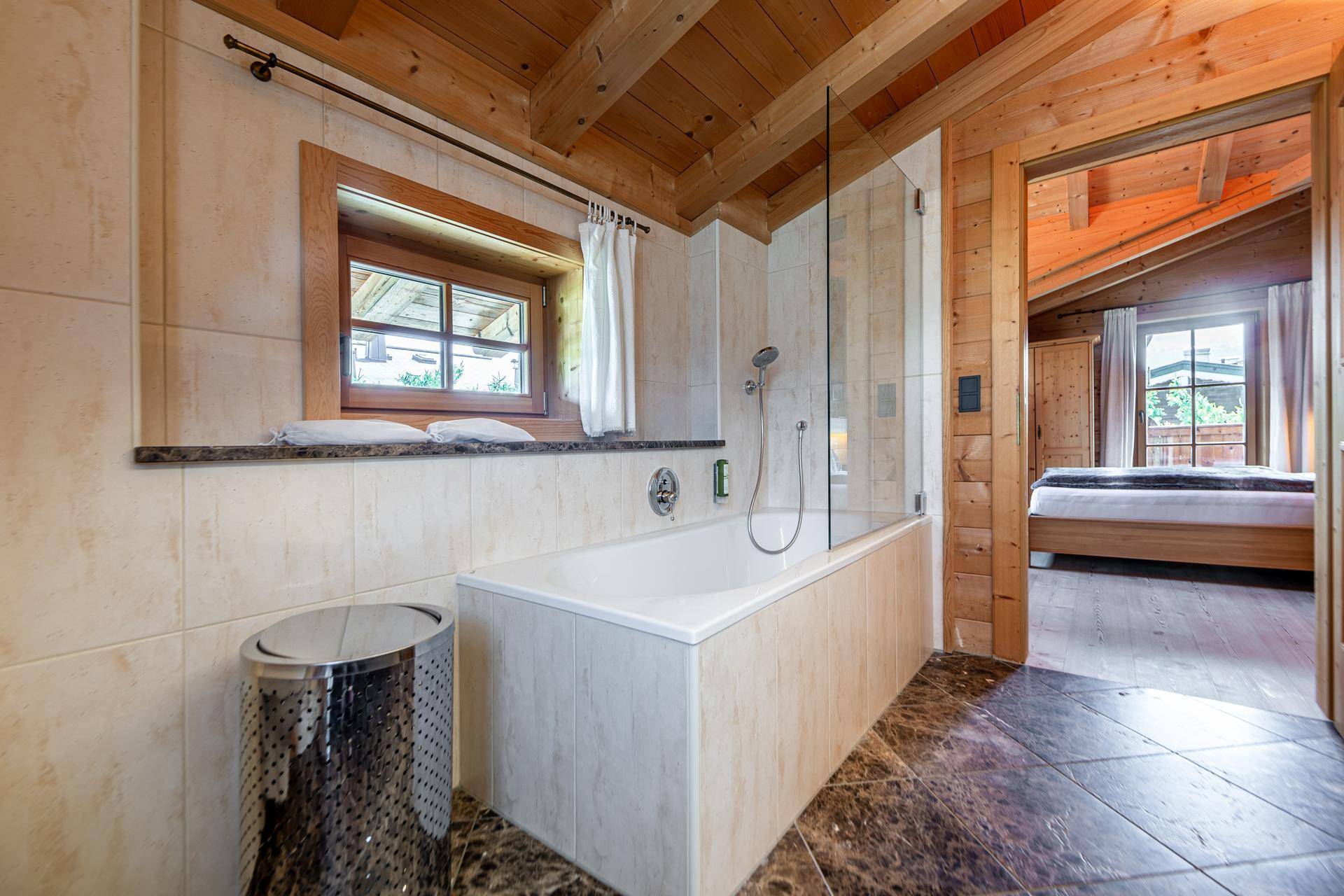 Badezimmer mit Badewanne, Dusche und Fenster, offen zum Schlafzimmer.