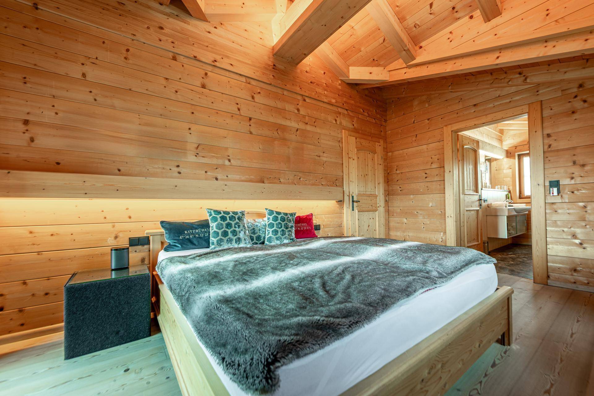 Helles Schlafzimmer mit Holzwänden, Holzboden und einem großen Doppelbett, offen zum Bad.