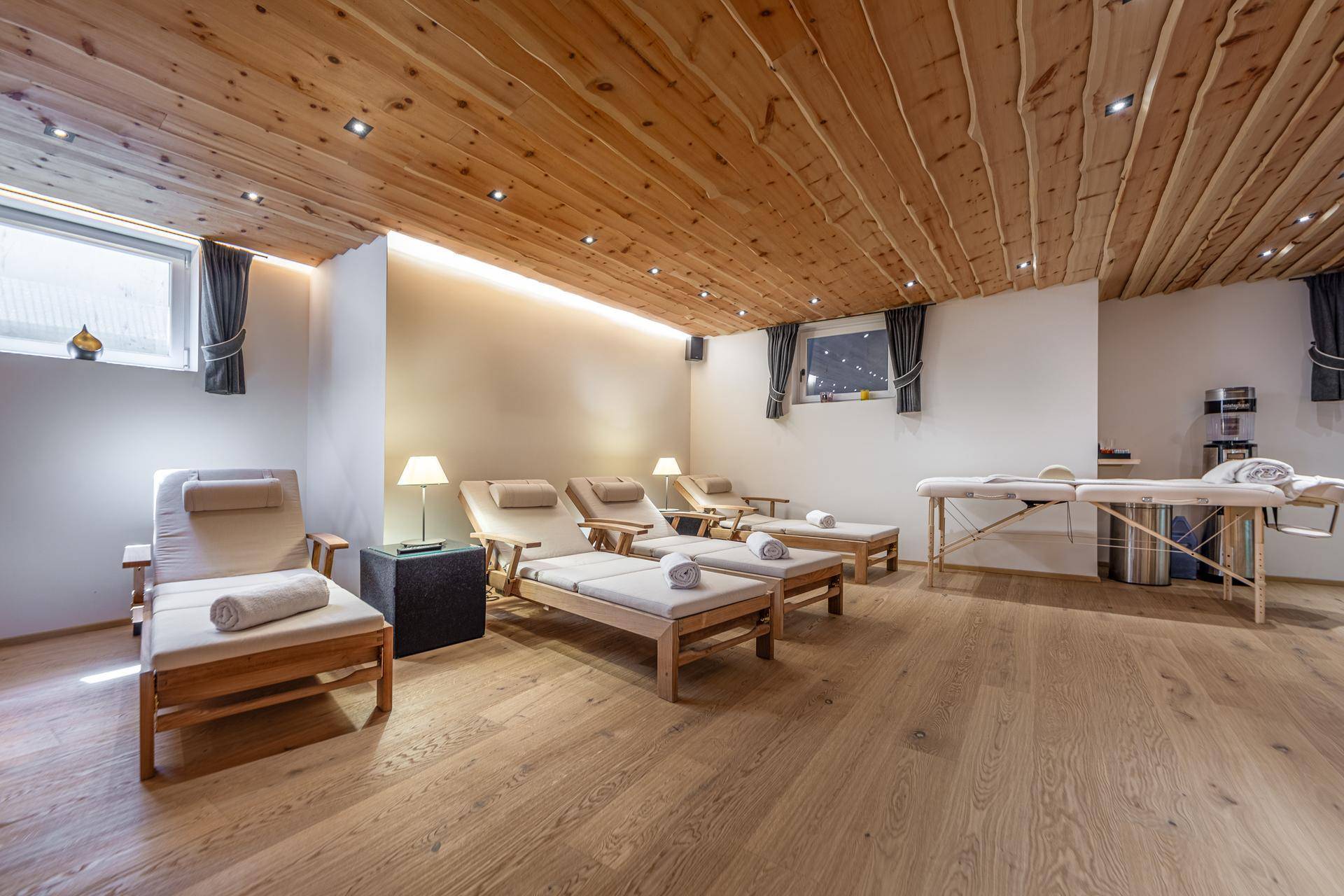 Geräumiger Wellnessbereich mit Liegestühlen, Massageliegen und Holzbalkendecke.