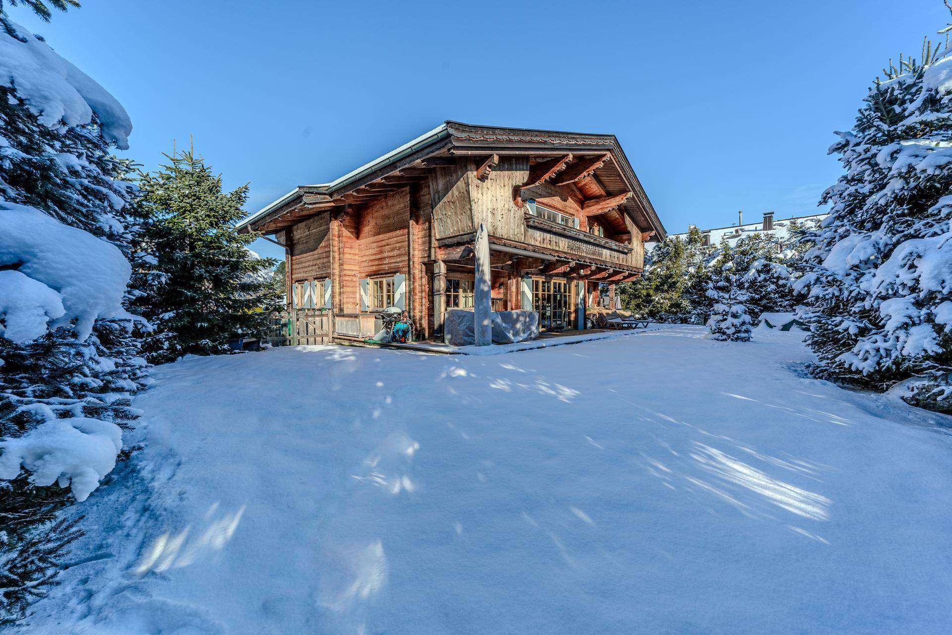 Charmantes Holzchalet im Winter, umgeben von schneebedeckten Bäumen und Bergen.