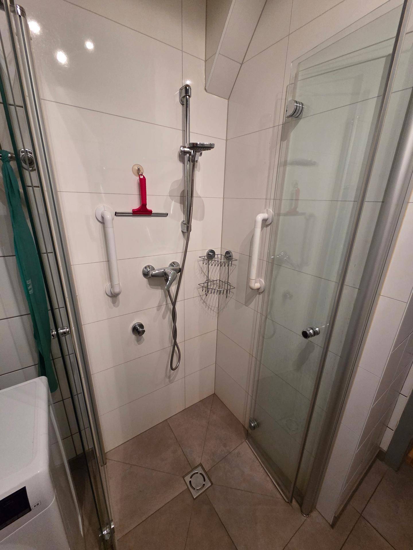 Modern geflieste Dusche mit Glasabtrennung und Haltegriffen für mehr Sicherheit.