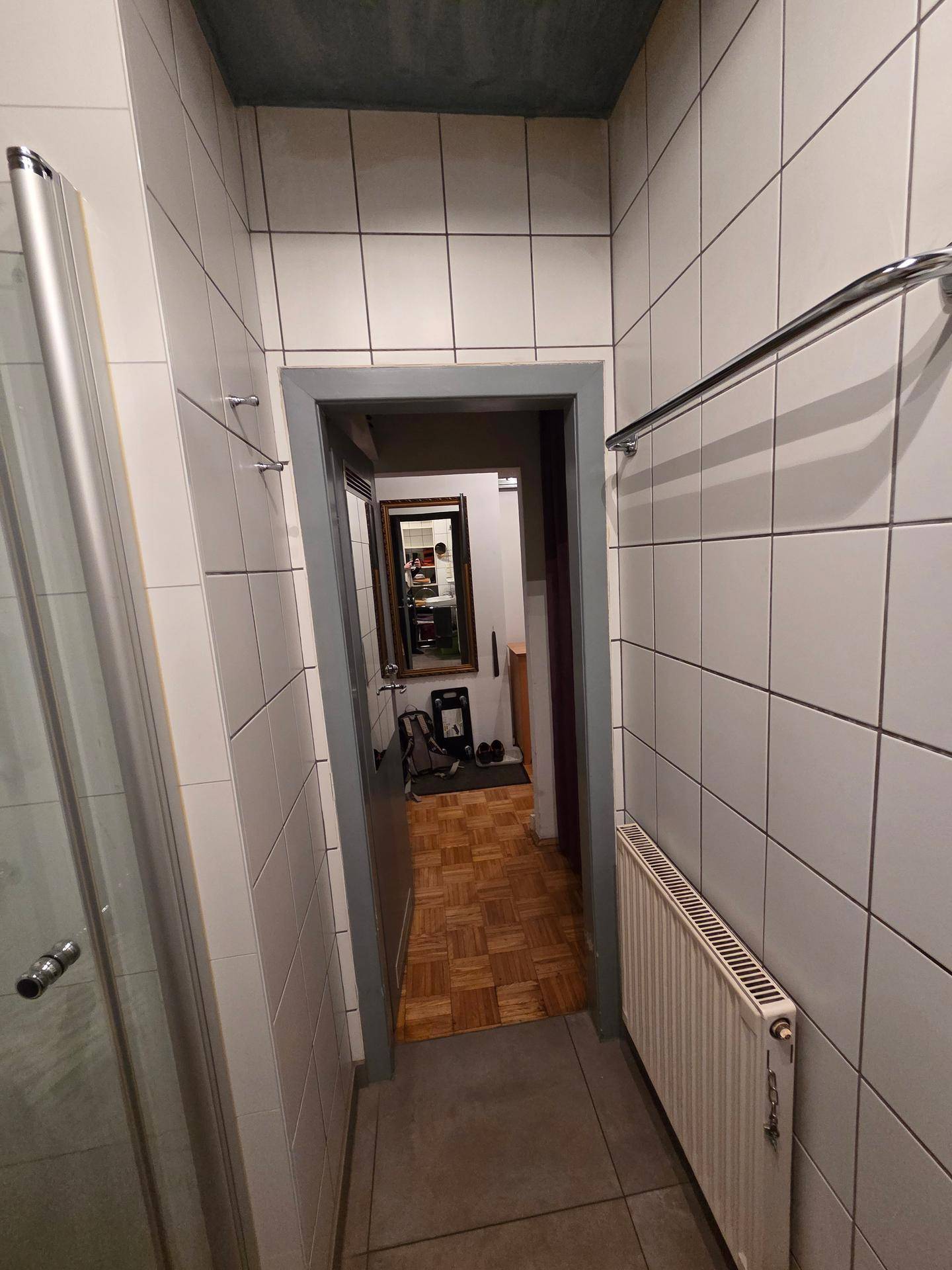Gefliester Flur mit Heizkörper und Blick in den angrenzenden Badezimmerbereich.