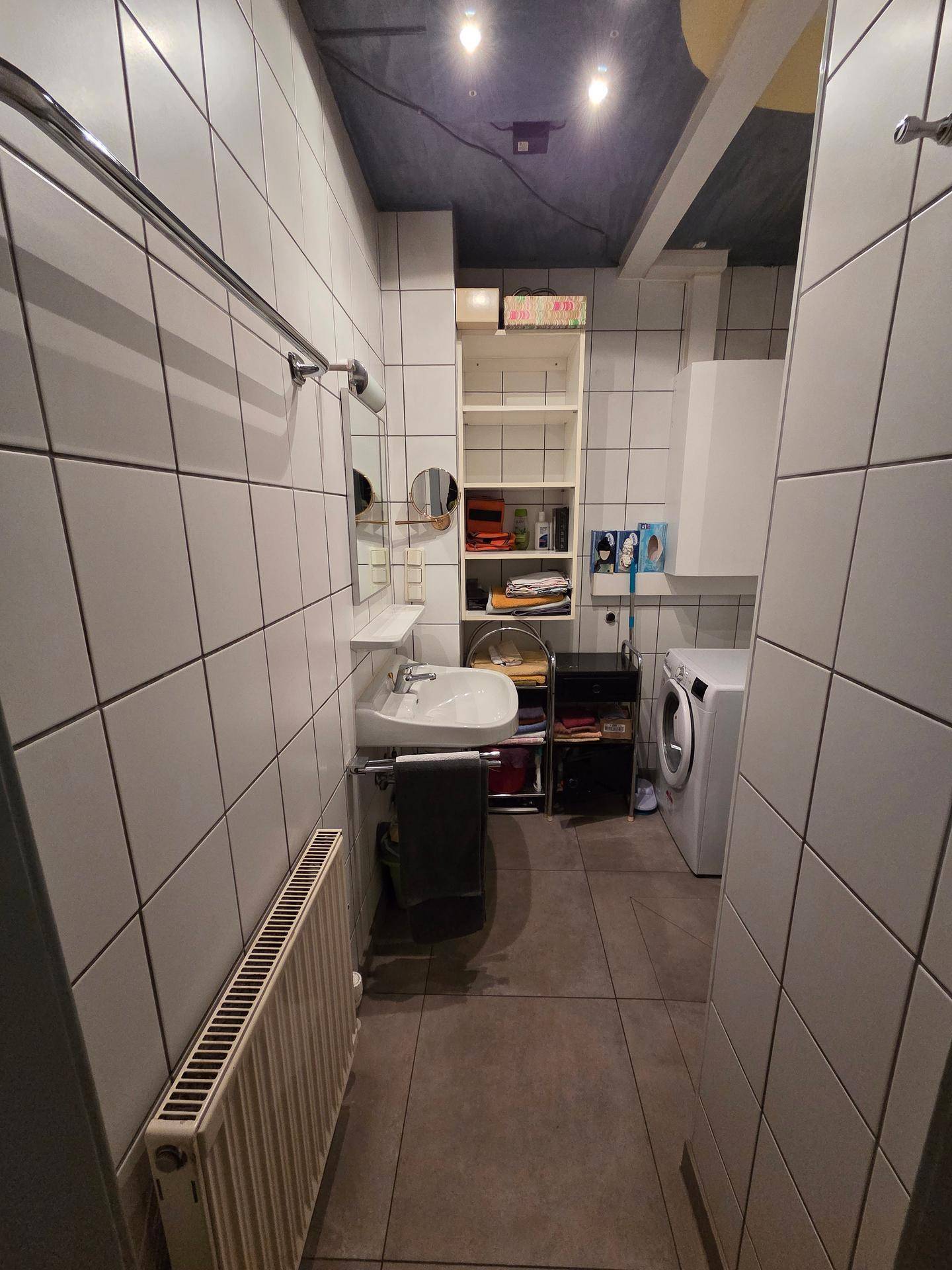 Badezimmer mit Waschbecken, Spiegel, Waschmaschine und weißen Wandfliesen.