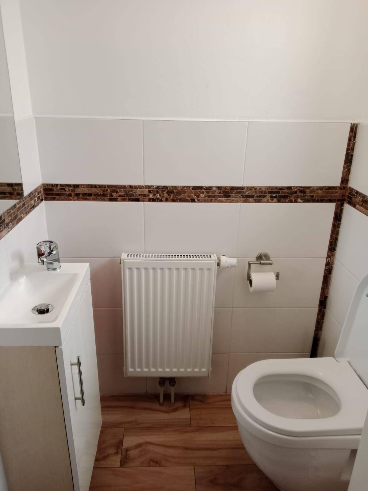 Kleines Gäste-WC mit weißen Fliesen, Waschbecken und Toilette.