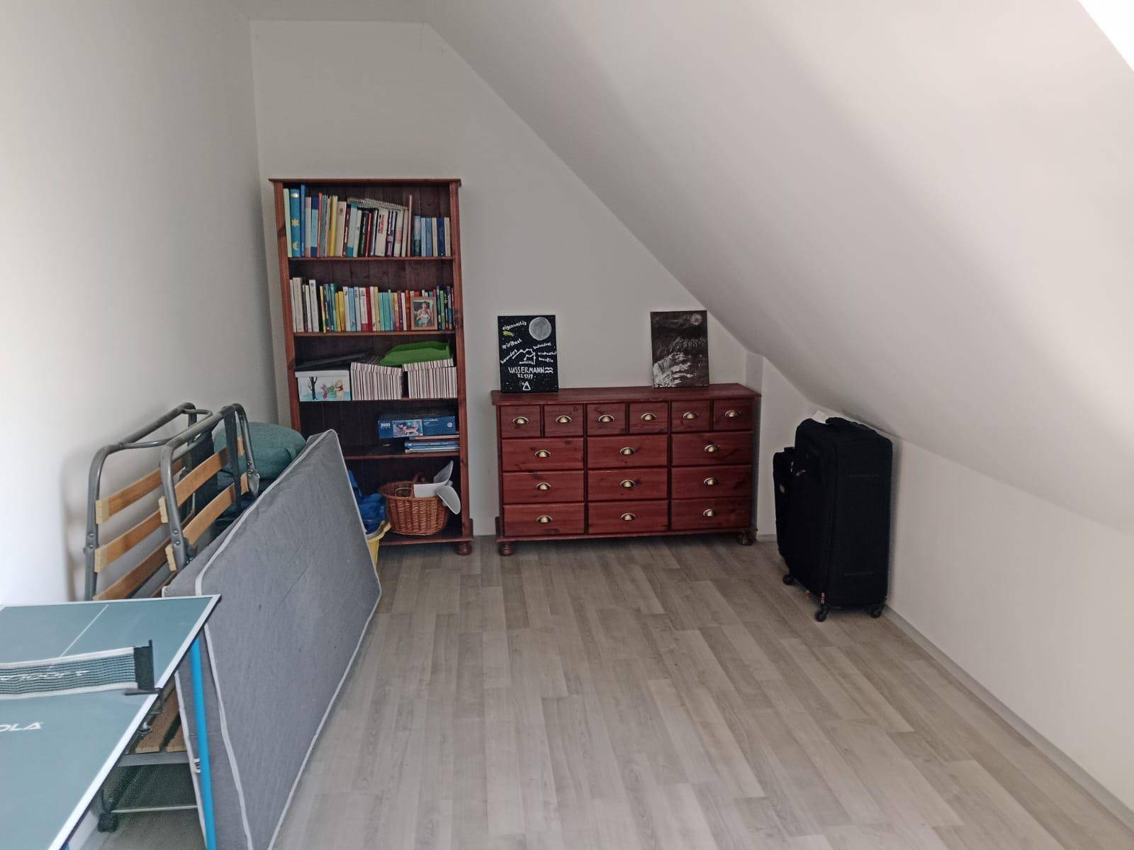 Dachgeschossraum mit Bücherregal, Kommode und Stauraum unter der Schräge.