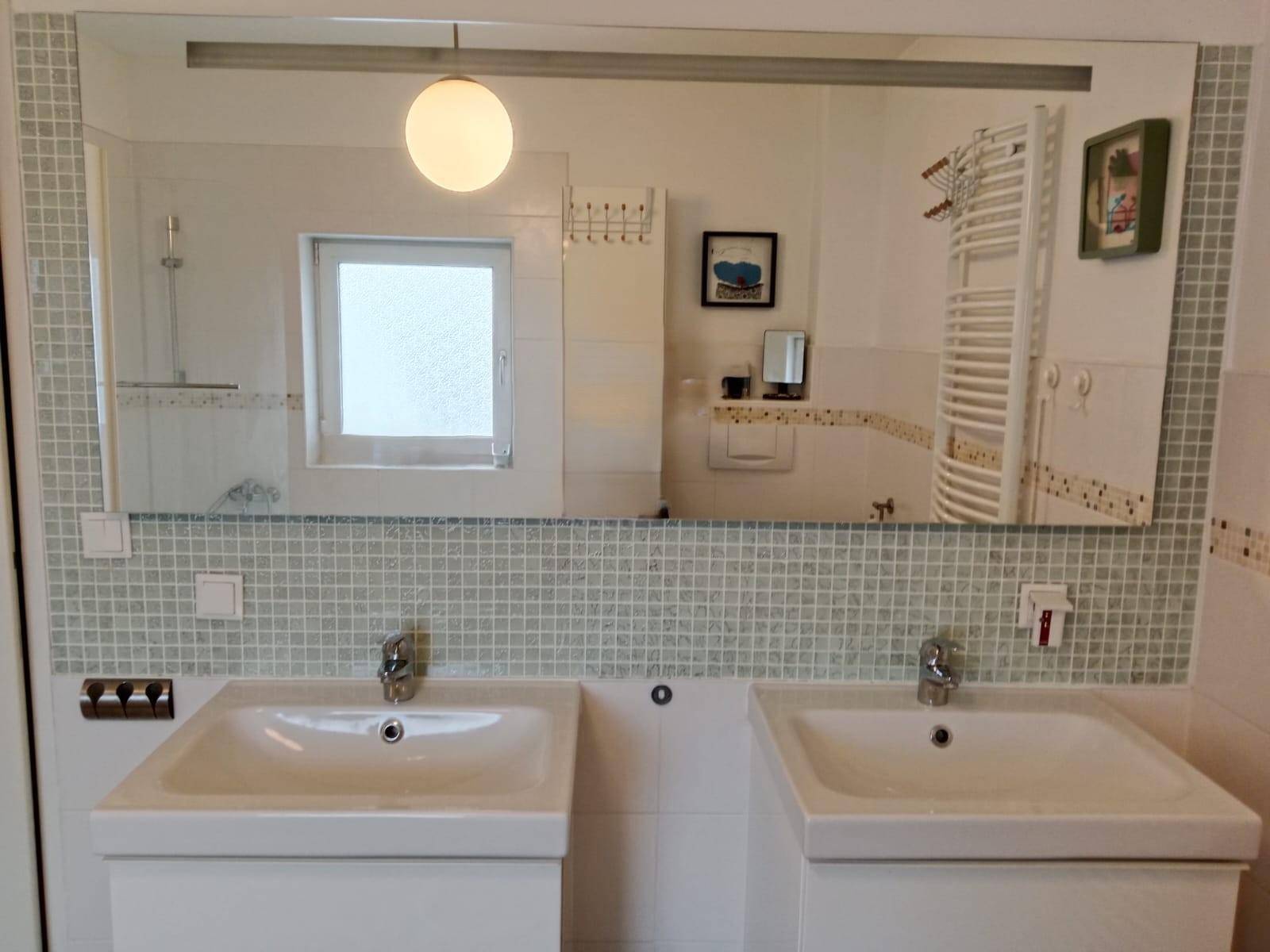 Badezimmer mit großem Spiegel, Doppelwaschbecken und Mosaikfliesen.