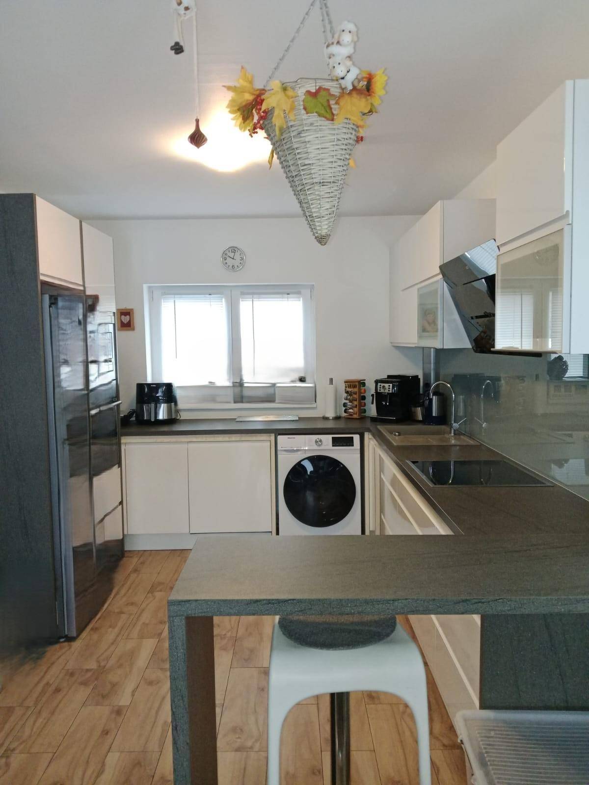 Moderne Küche mit weißen Schränken, dunkler Arbeitsplatte und integrierter Waschmaschine.