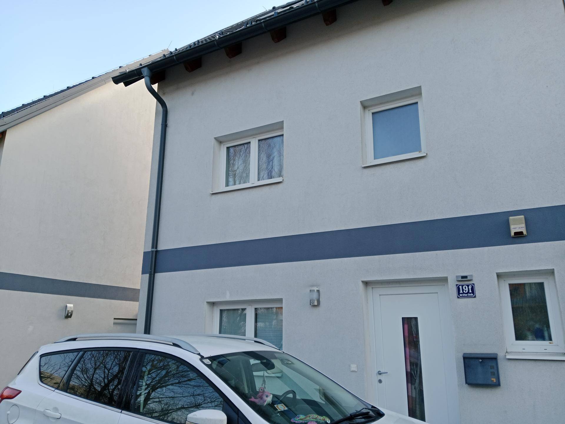 Vorderansicht eines Reihenhauses mit weißer Eingangstür und Fenstern.
