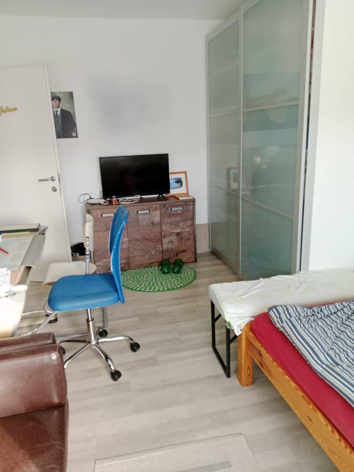 Schlafzimmer mit Bett, Schreibtisch, Bürostuhl und einem modernen Kleiderschrank.