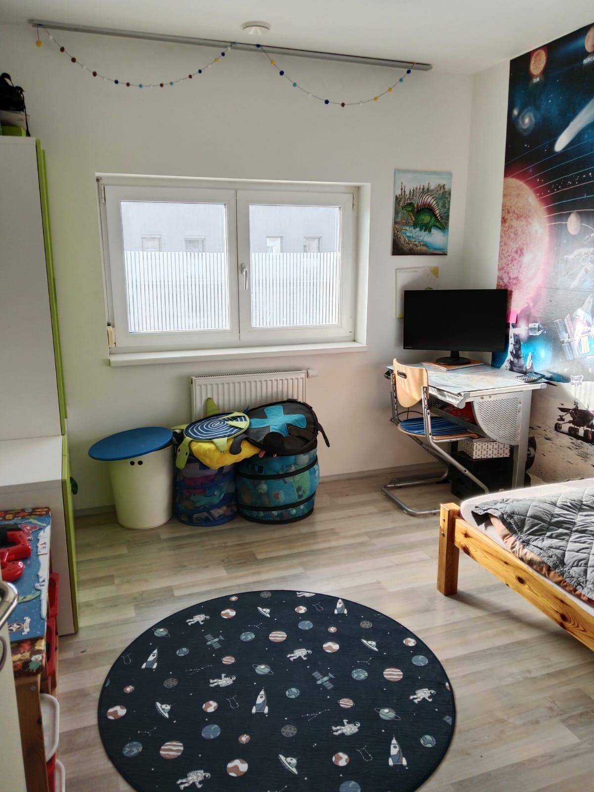 Kinderzimmer mit Bett, Schreibtisch und farbenfroher Dekoration an den Wänden.